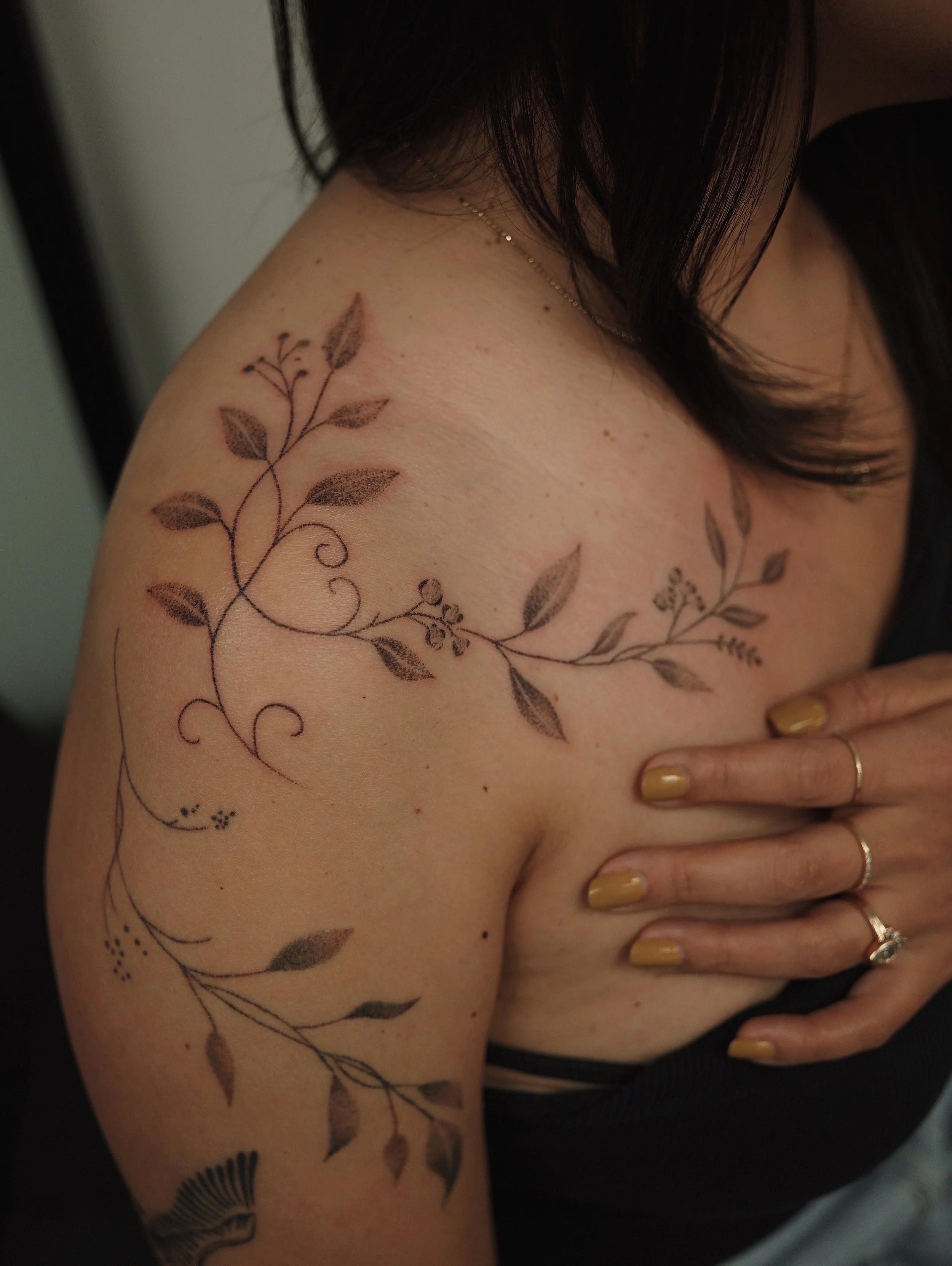 Tattoo of leafy vines and floral designs on a woman's shoulder and upper arm.