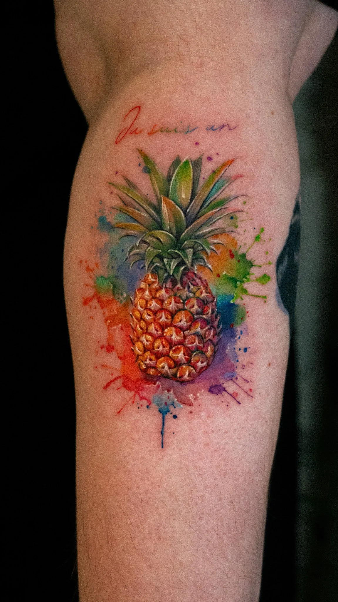 Colorful tattoo of a pineapple with watercolor splashes and the phrase 'Juice is an' written above.