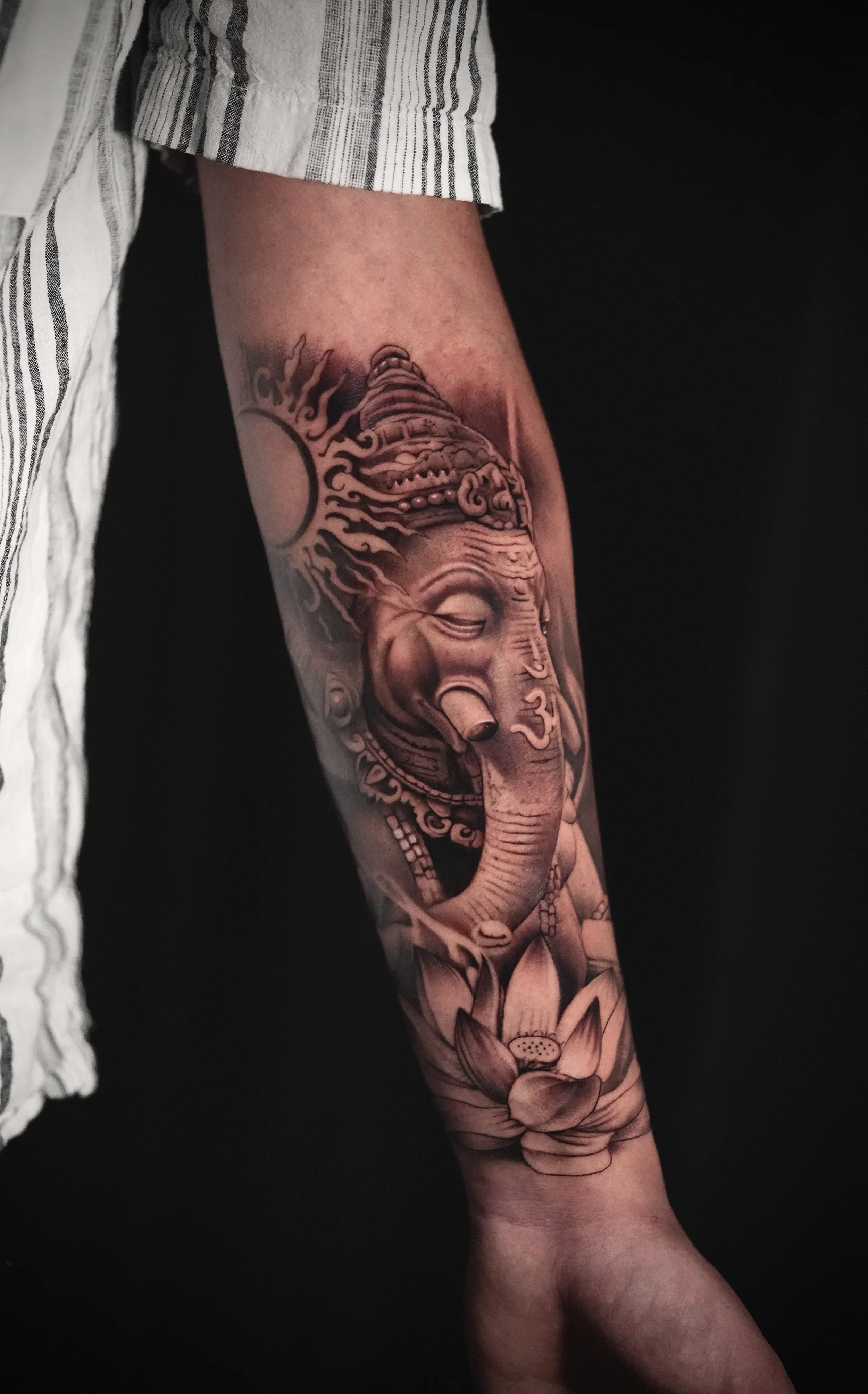 Tattoo of Lord Ganesha on a person's forearm, featuring Ganesha's face, an elephant head with a lotus flower at the bottom, and decorative elements.
