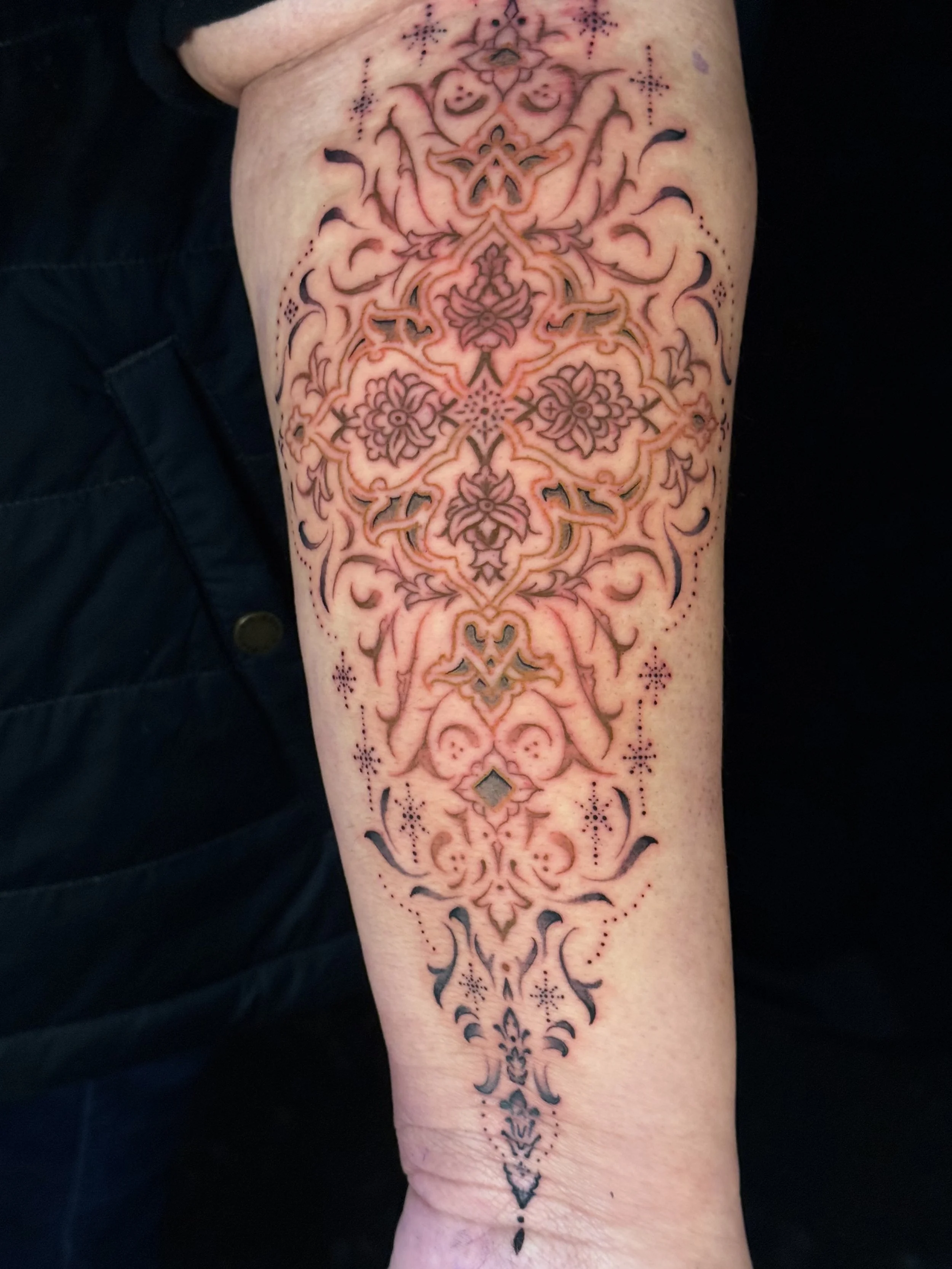 Ornate tattoo with intricate floral and symmetrical patterns extending down a person's forearm.