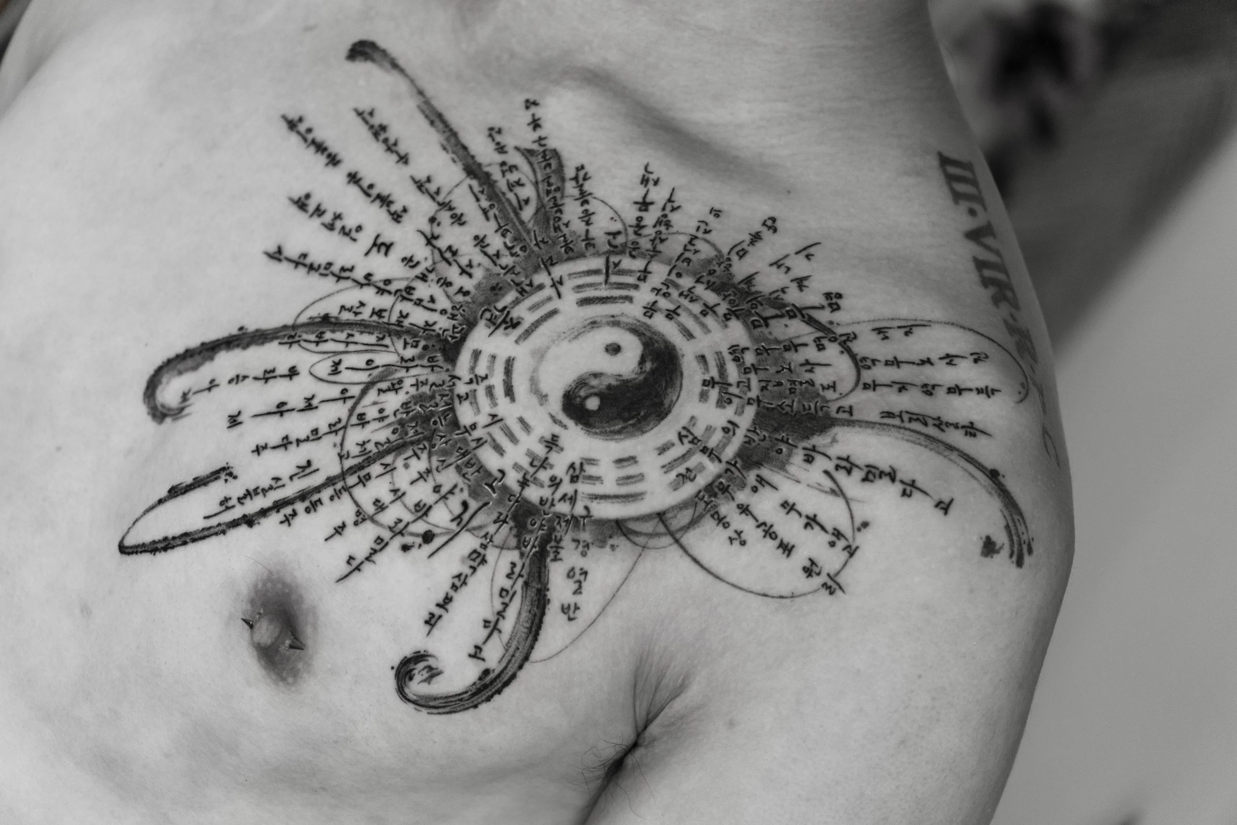 Black and white tattoo on a person's chest featuring a yin-yang symbol at the center, with a spider-web design and Asian script surrounding it.