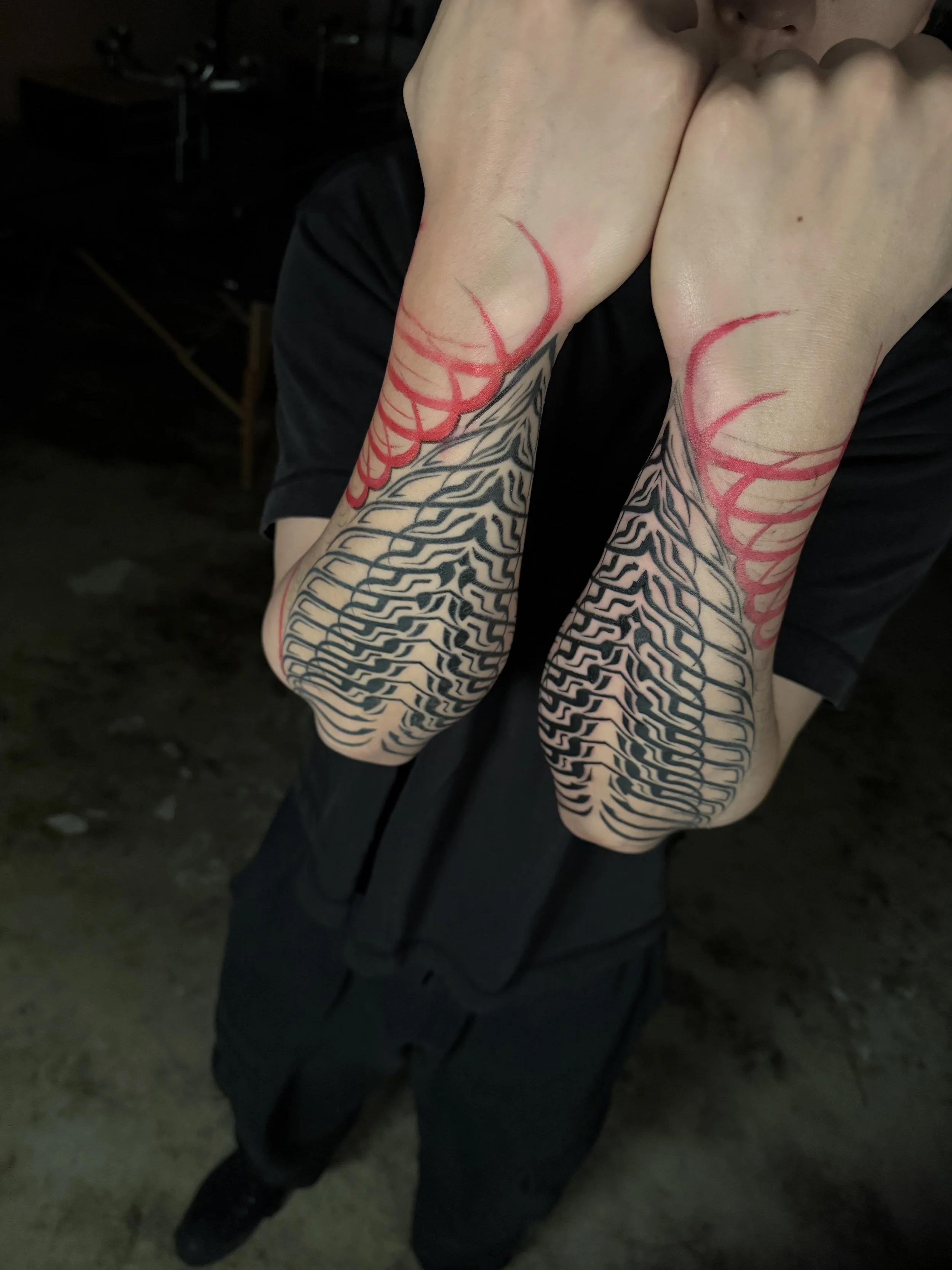 Person with detailed black and red tattoo sleeves on both arms, with the sleeves featuring intricate patterns, covering from the shoulders to the wrists, while the individual is sitting with arms crossed in front of their face.