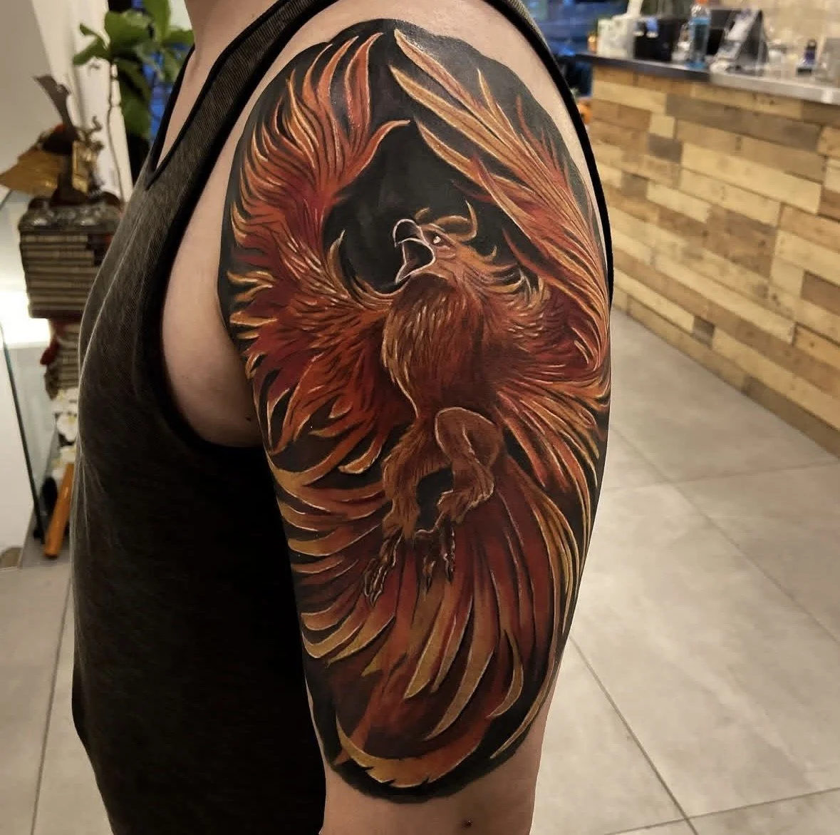 Tattoo of a fiery red and orange phoenix bird with its wings spread wide on a person's upper arm.