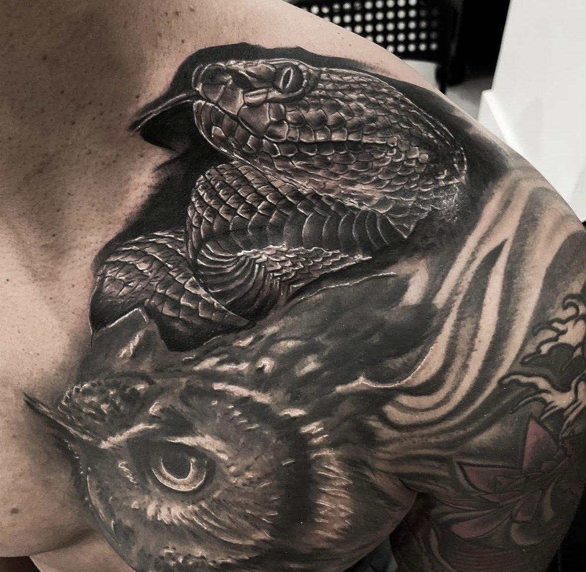 Black and gray tattoo of a snake and an owl on a person's shoulder and upper arm.