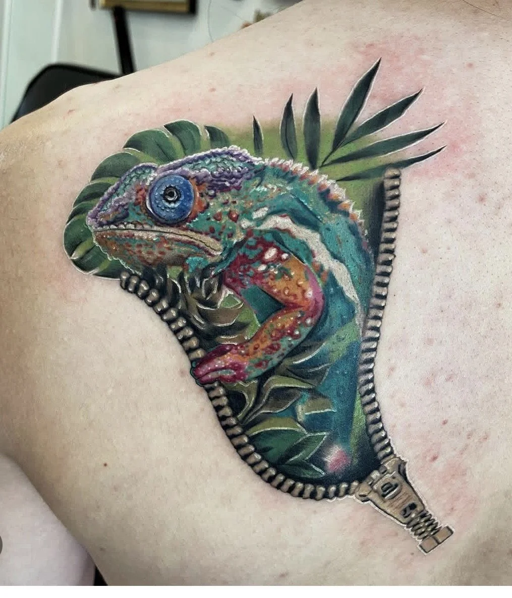 A colorful tattoo of a chameleon partially unzipped, revealing tropical leaves behind it.
