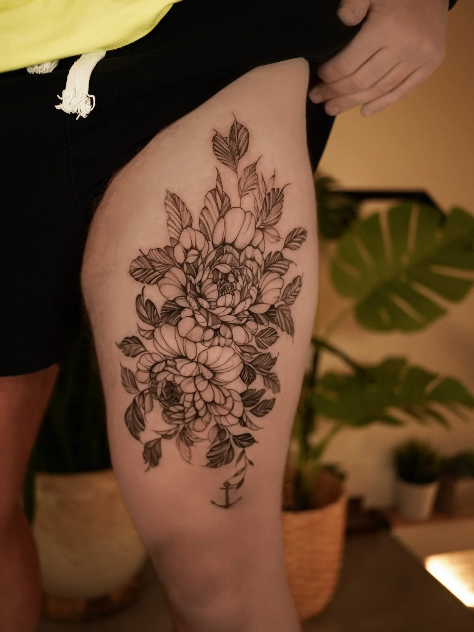A black ink floral tattoo of large flowers with detailed leaves on a person's upper thigh.