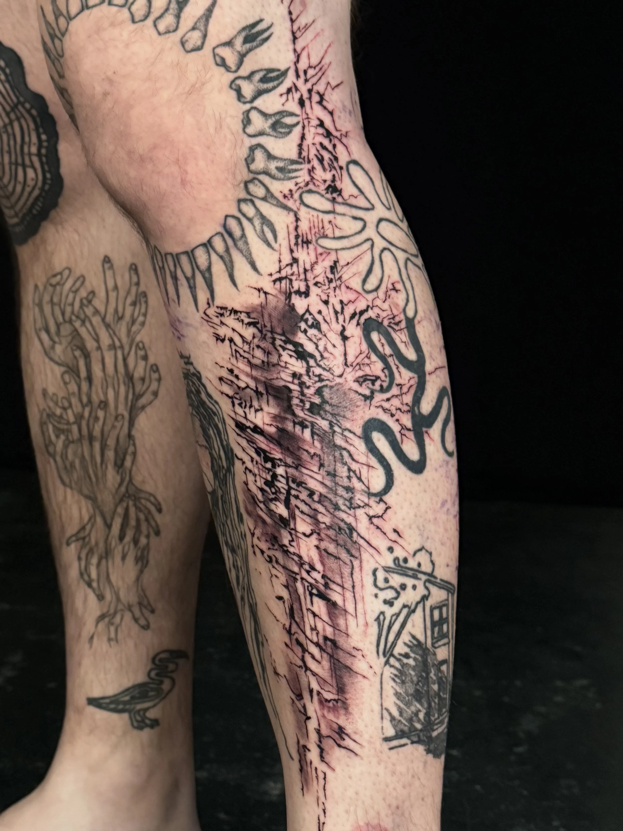 Tattooed arm with various designs, including black ink snakes, trees, and abstract patterns in progress.