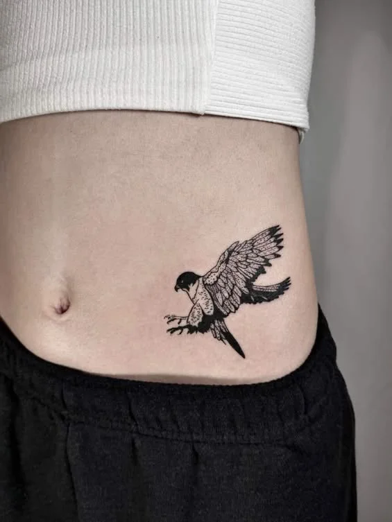 Tattoo of a bird with detailed wings on a person's lower abdomen.