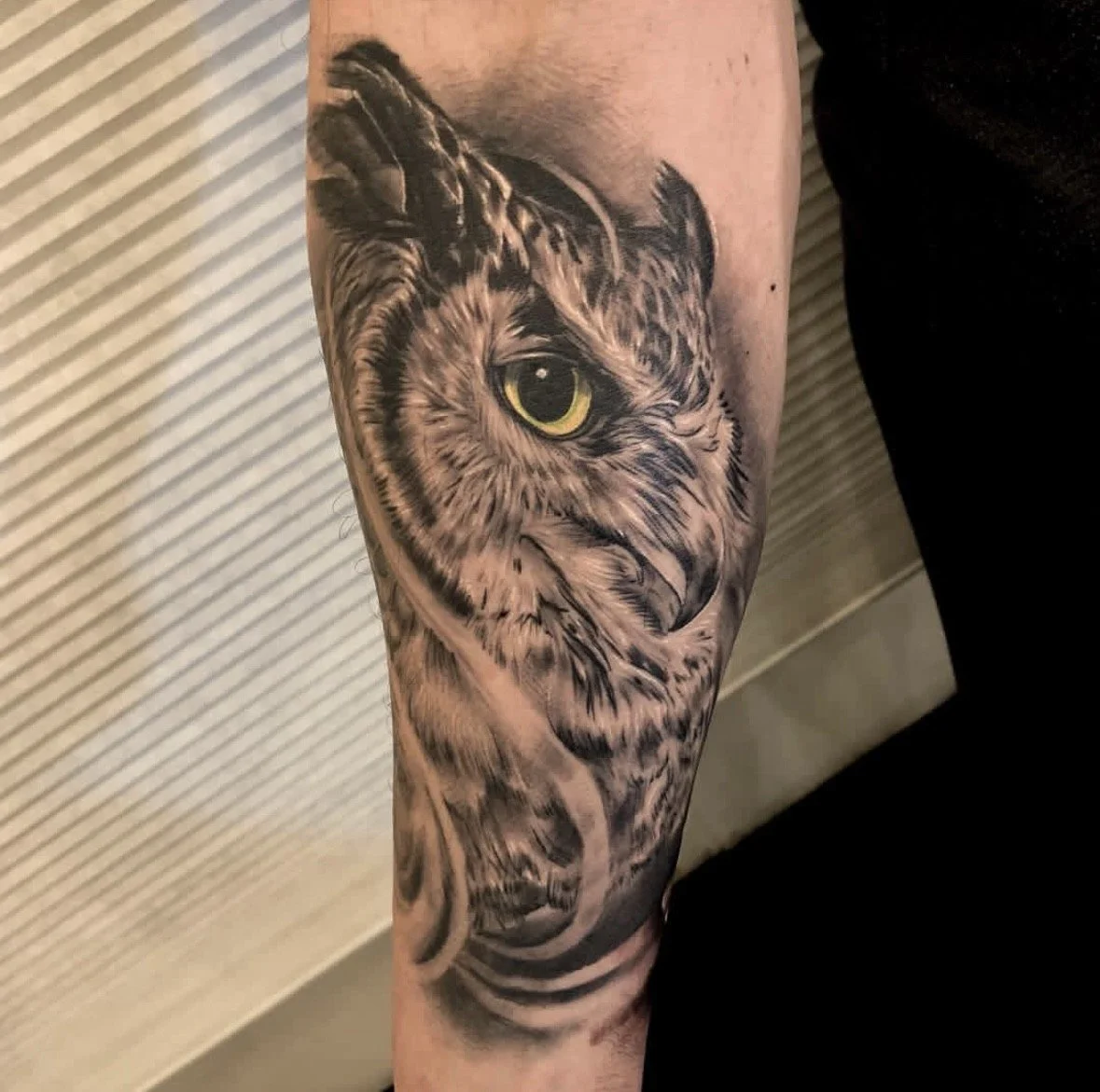 Black and gray tattoo of a tiger's face with a yellow eye on a person's arm.