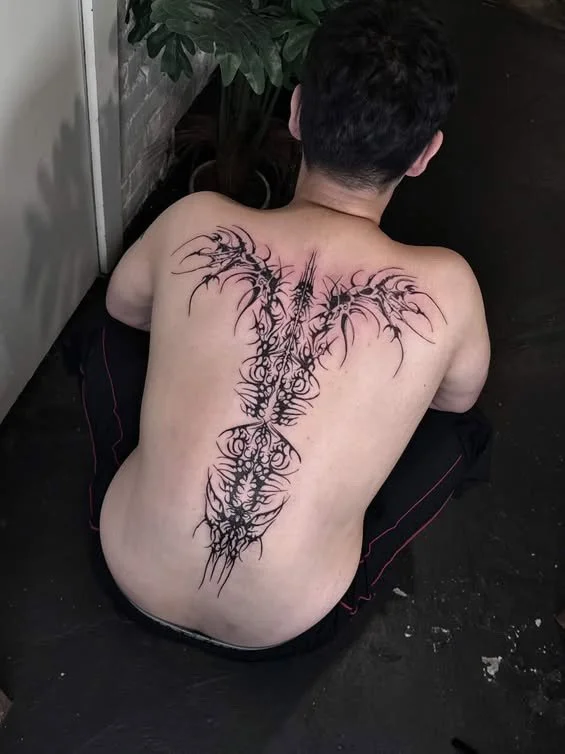 Back view of a person with a large, intricate tribal-style tattoo resembling a dragon or mythical creature running down their back from shoulders to lower back.