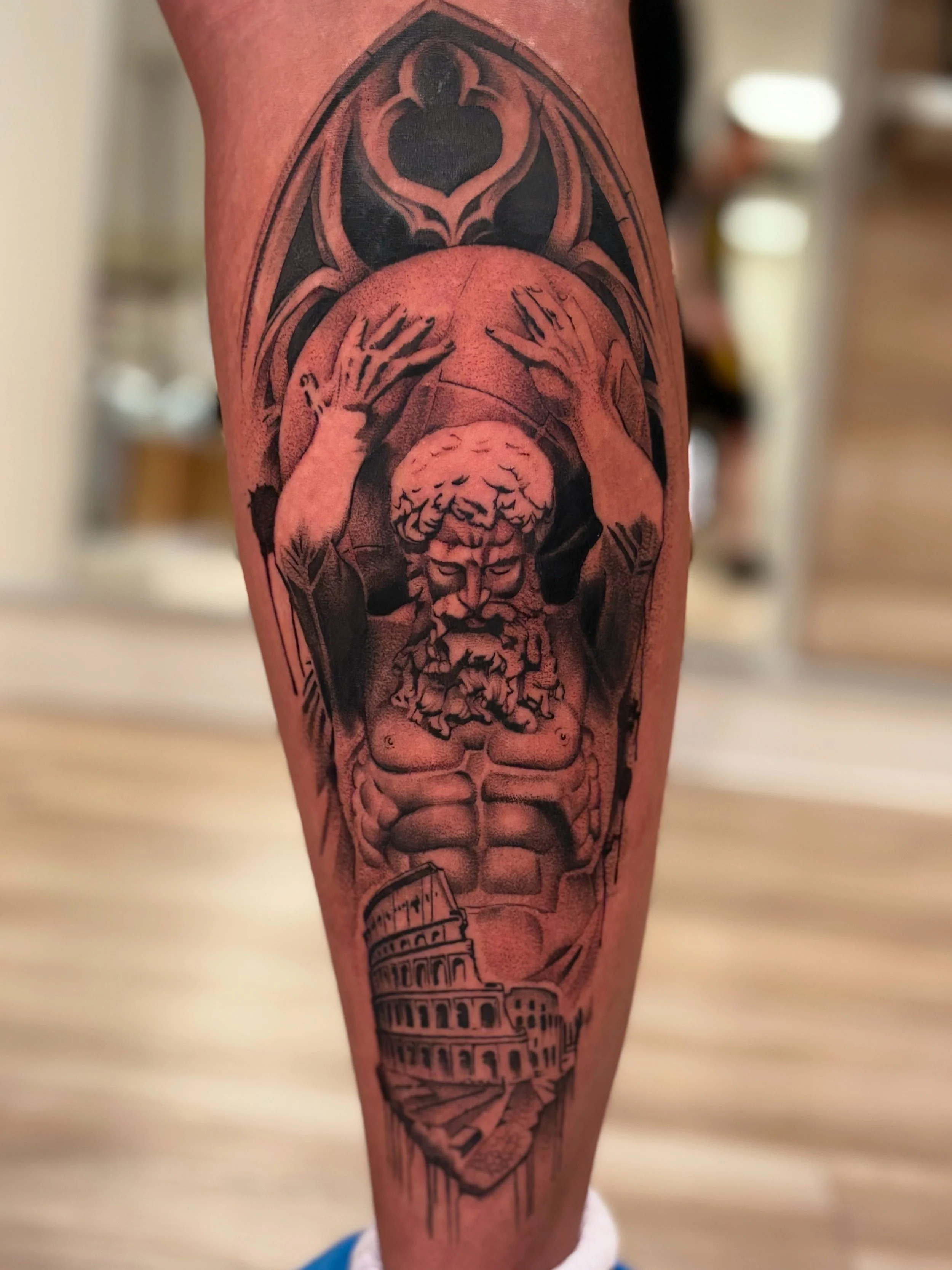 Tattoo of an ancient god with a beard raising his hands, with a background of a stained glass window and the Roman Colosseum.