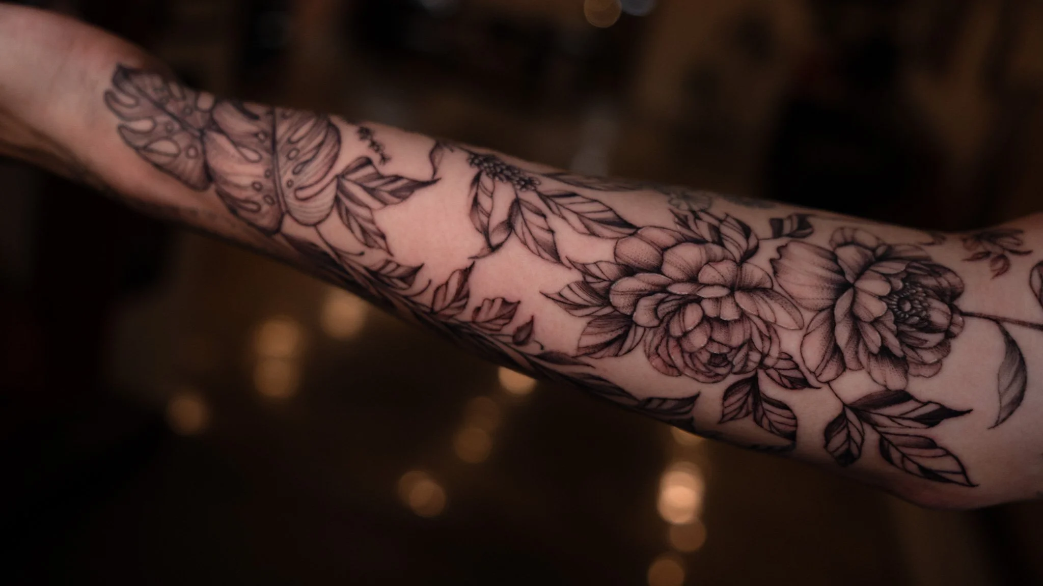 A close-up of a person's arm with a detailed black and gray floral tattoo design.