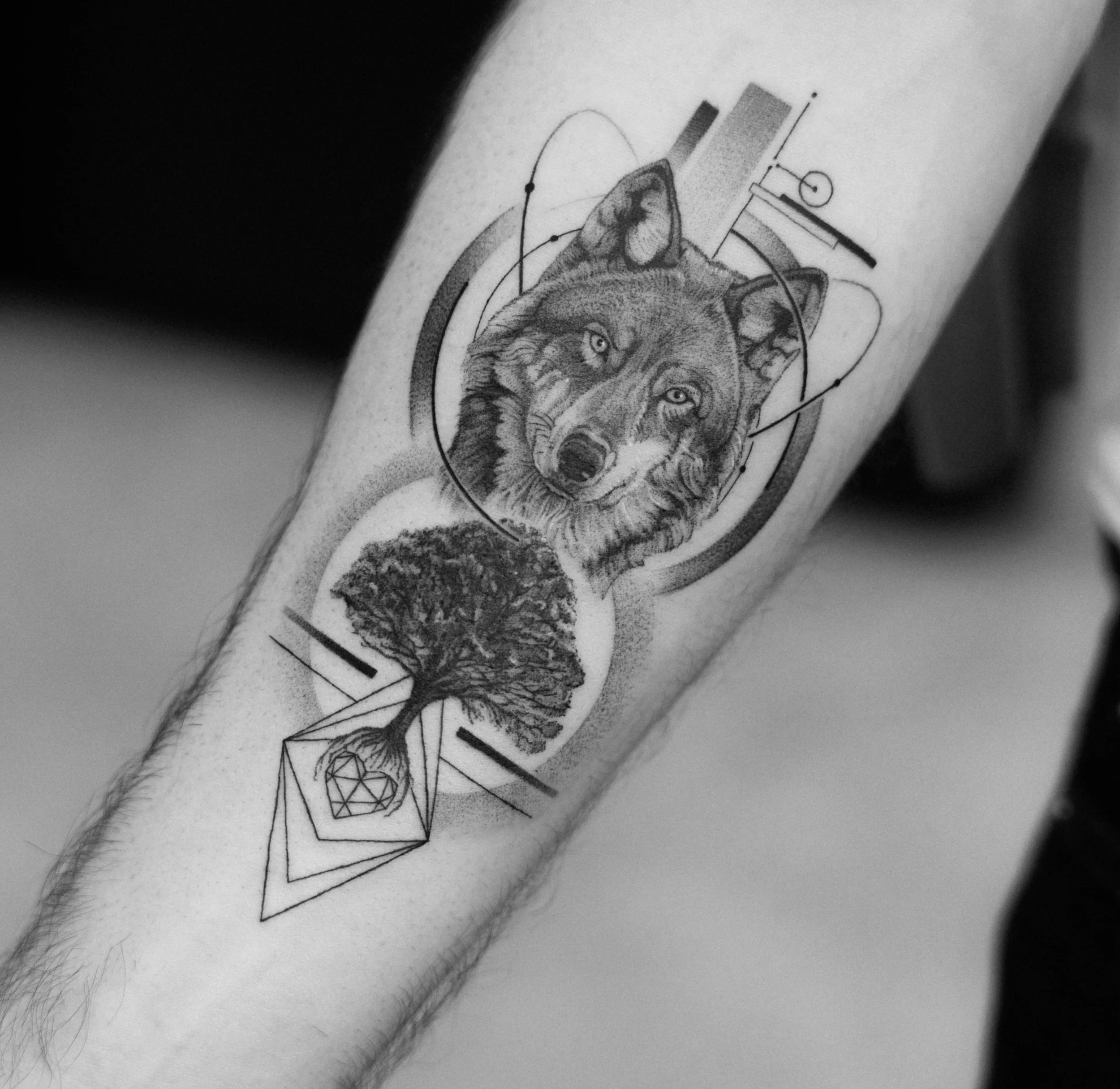 Tattoo of a wolf's face, a tree scene, and geometric elements with abstract lines and shapes.