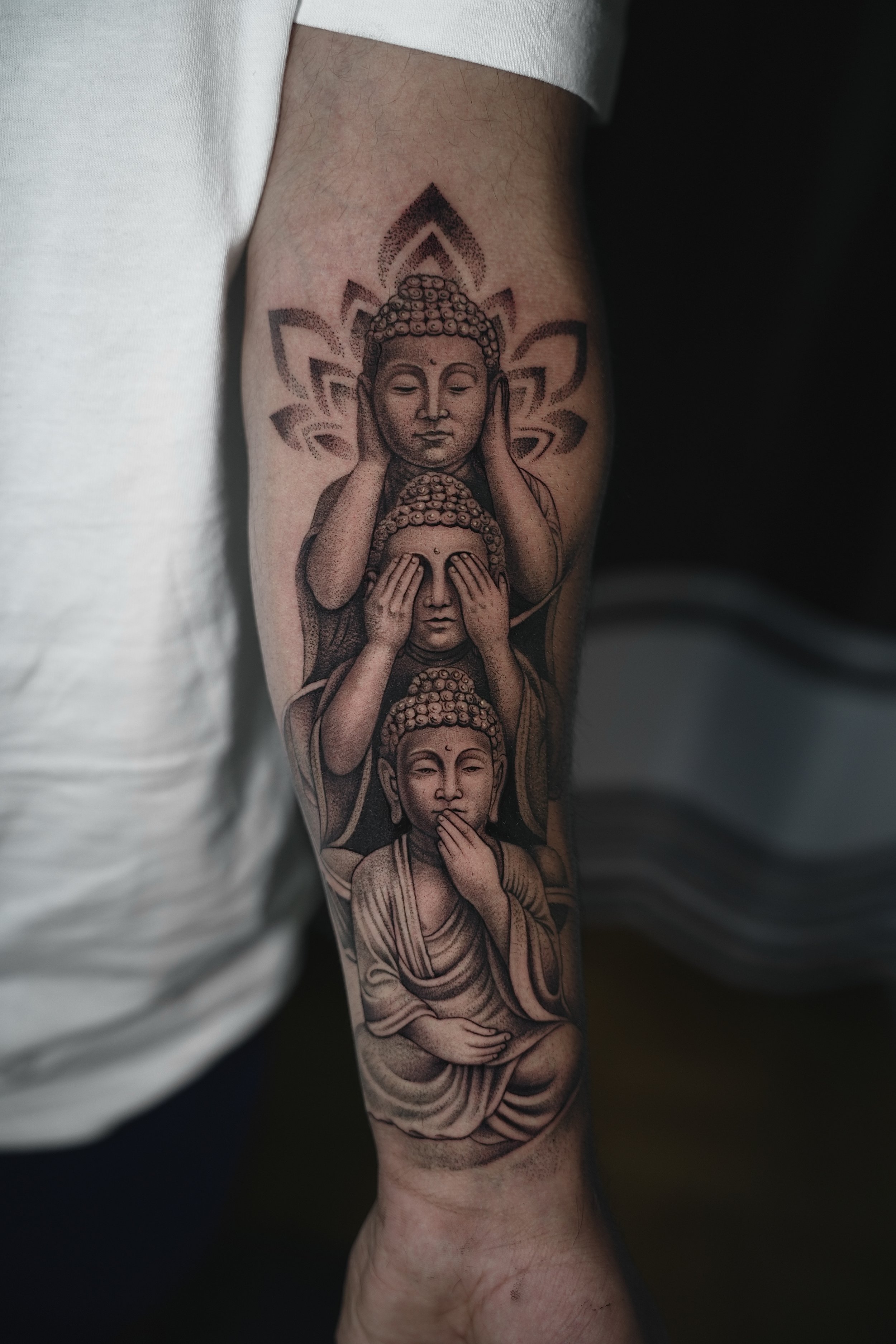 Tattoo of three Buddhist figures stacked vertically on a person's arm, with a lotus design in the background.