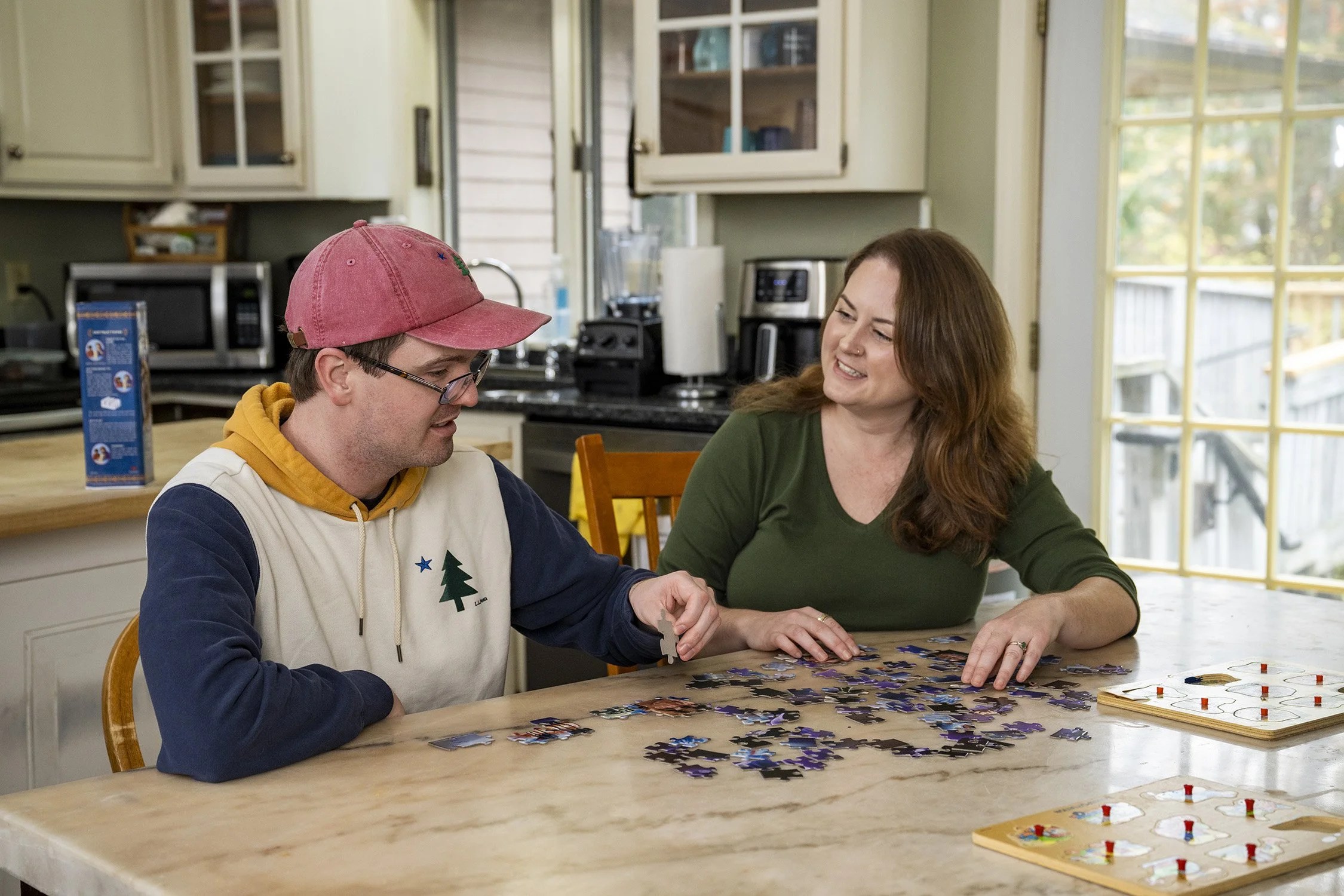 A Casa client and SLP sit at a kitchen table and enjoy doing a puzzle together