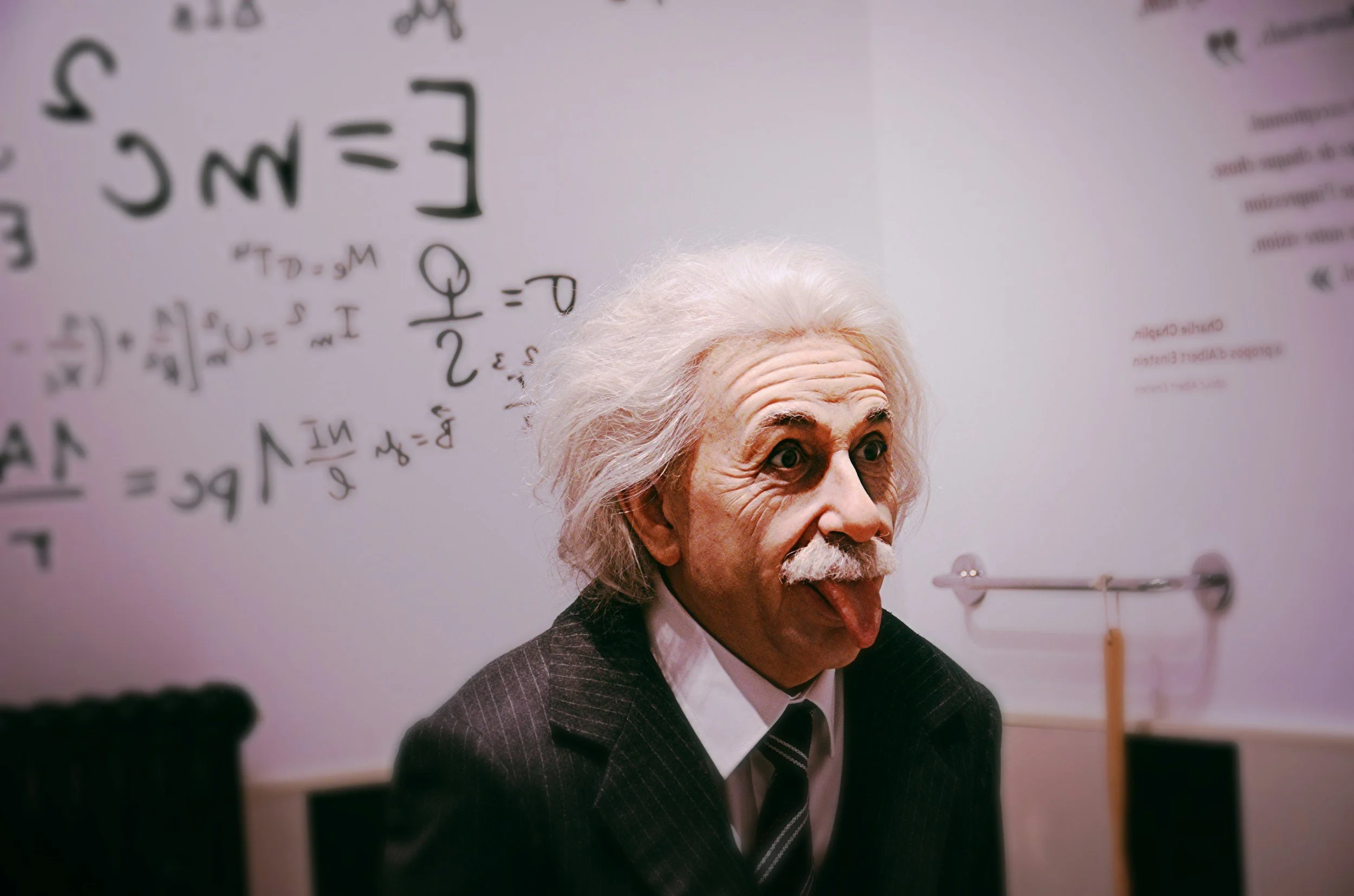 An image of what appears to be Einstein in a classroom in front of white board, with his tongue sticking out. 