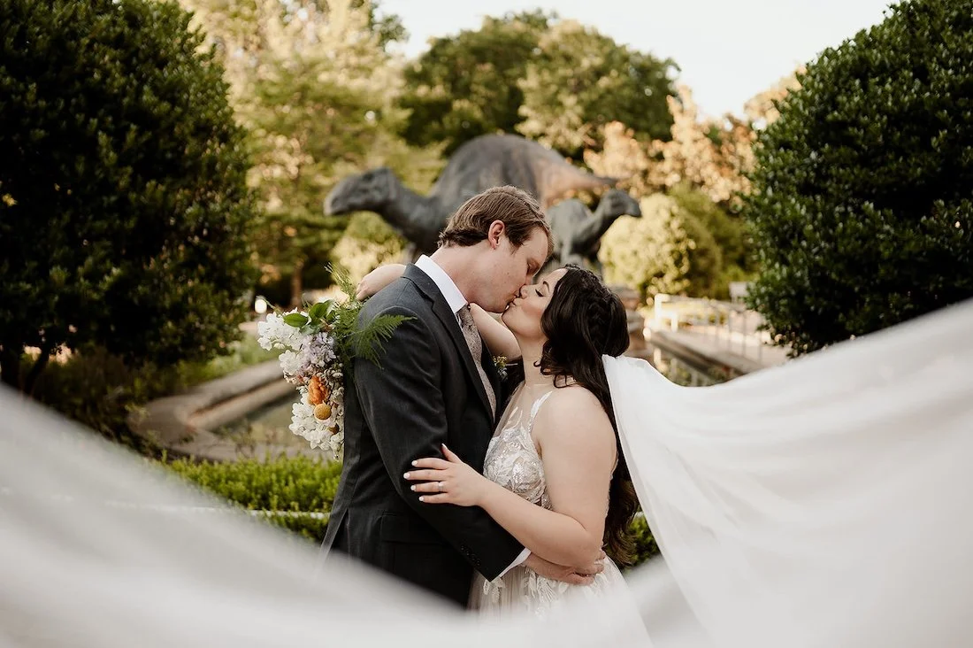 bride and groom kiss in front of a historic statue at the fernbank museum