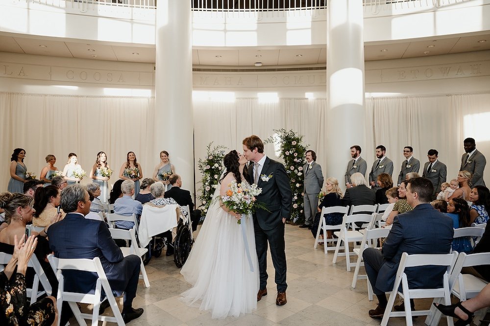 bride and groom share a kiss after they say i do inside the fernbank museum of natural history in atlanta ga