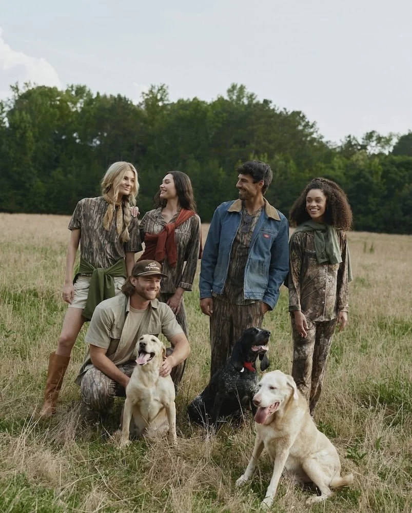 men and women standing outside in a field with dogs and wearing camo