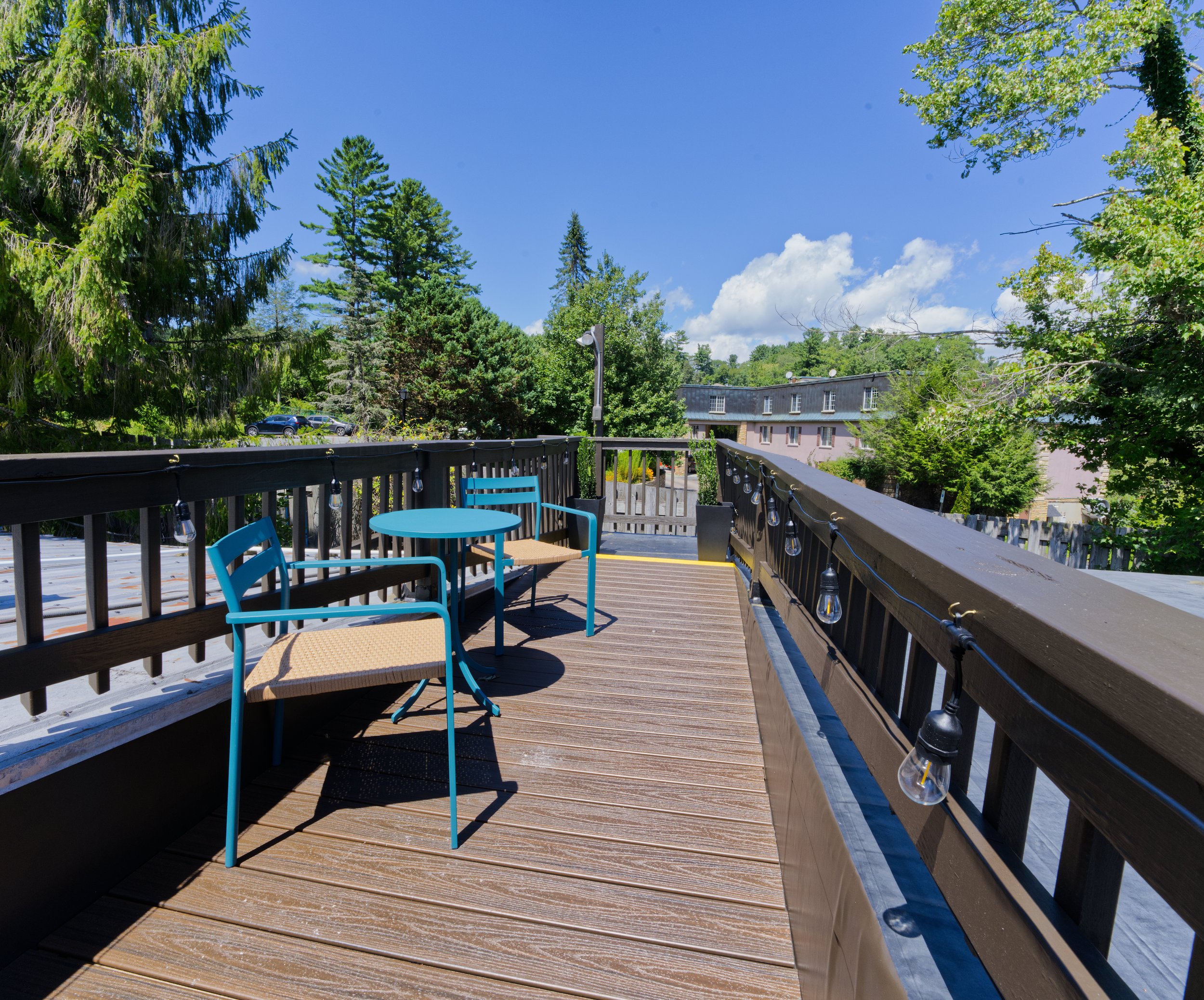 Balcony with blue chairs, string lights, overlooking a parking lot and green trees under a clear blue sky.