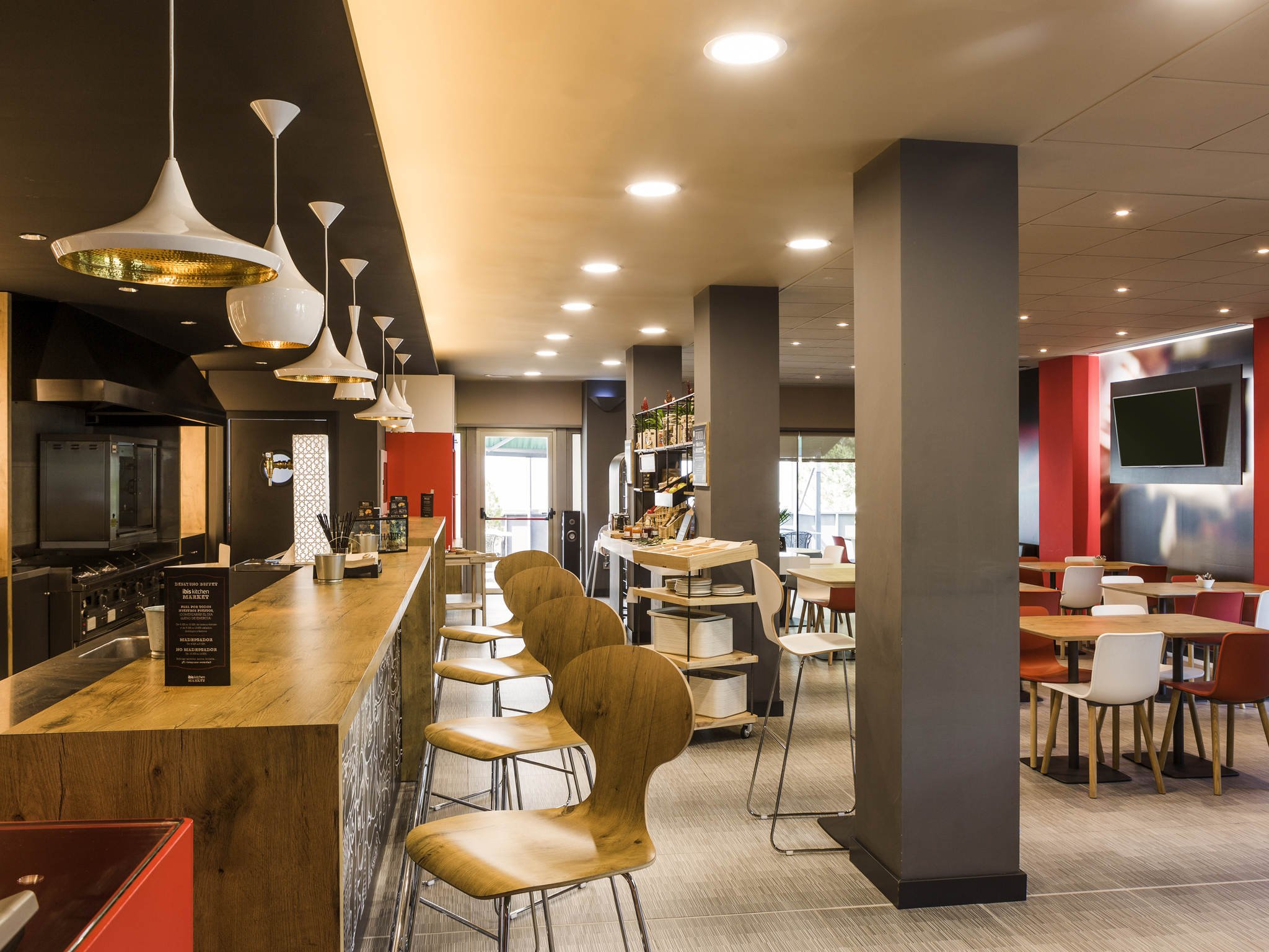 Interior of a modern restaurant or cafe with wooden bar counter, high chairs, and various seating arrangements, illuminated by ceiling lights and pendant lamps.