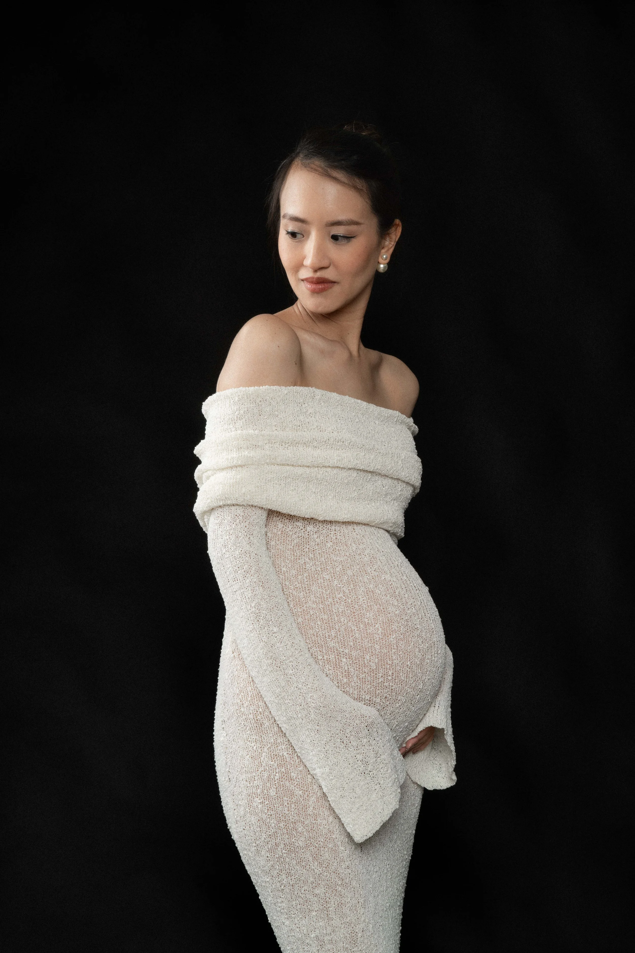 Christina in a flowing dress, full-length maternity portrait against a dark, black backdrop