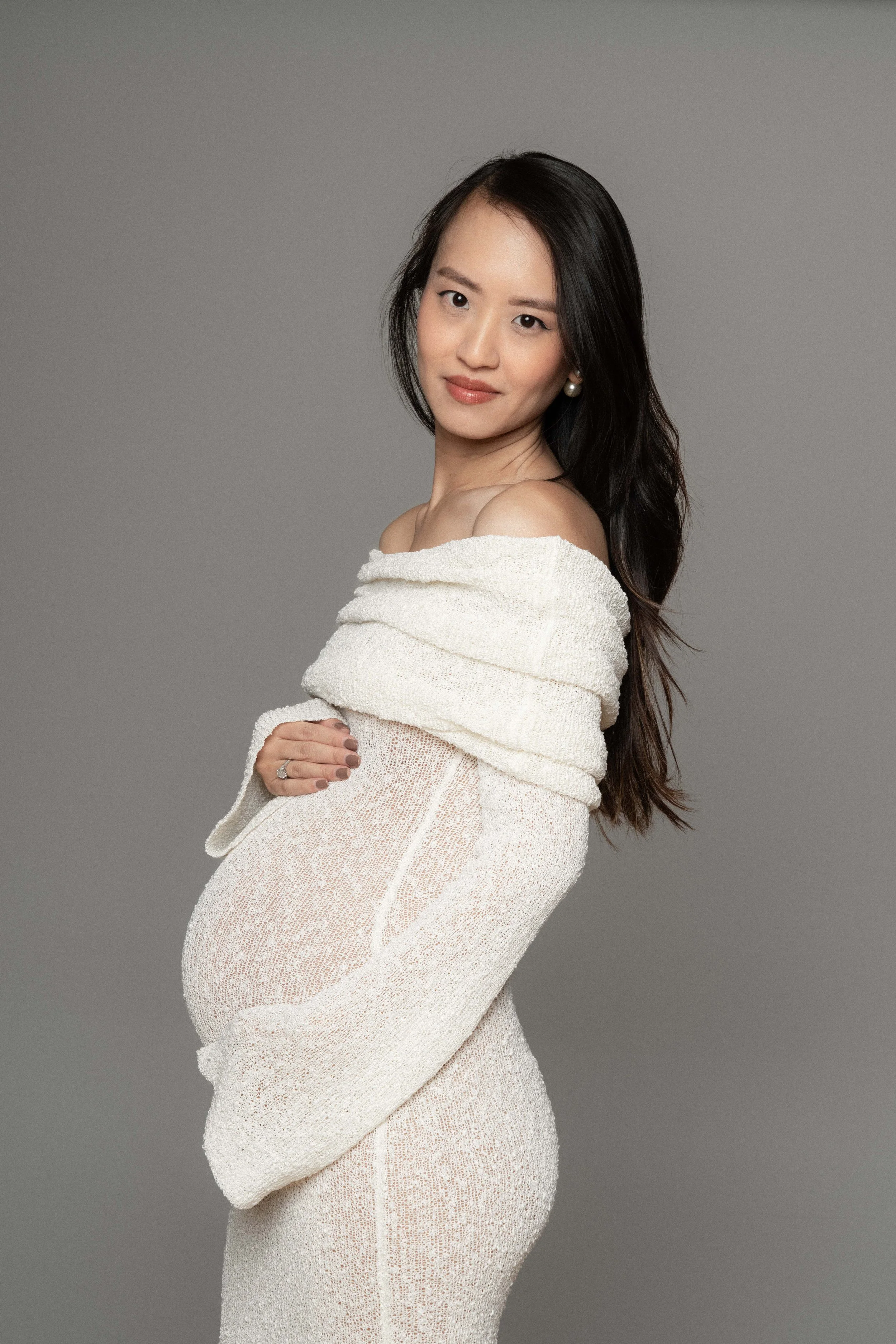 Christina's profile in a flowing dress, maternity portrait against a neutral backdrop