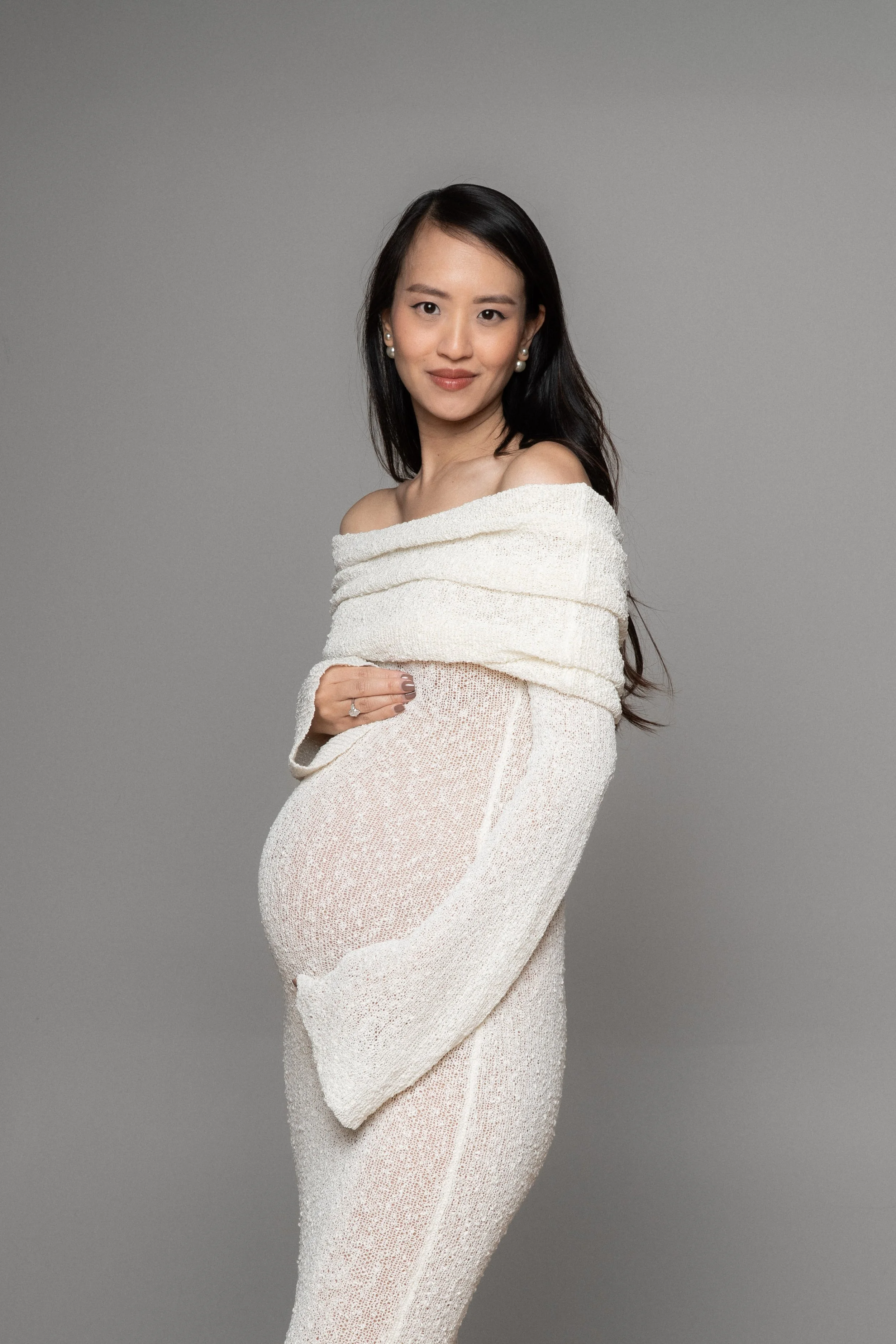Christina in a flowing dress, full-length maternity portrait against a neutral backdrop