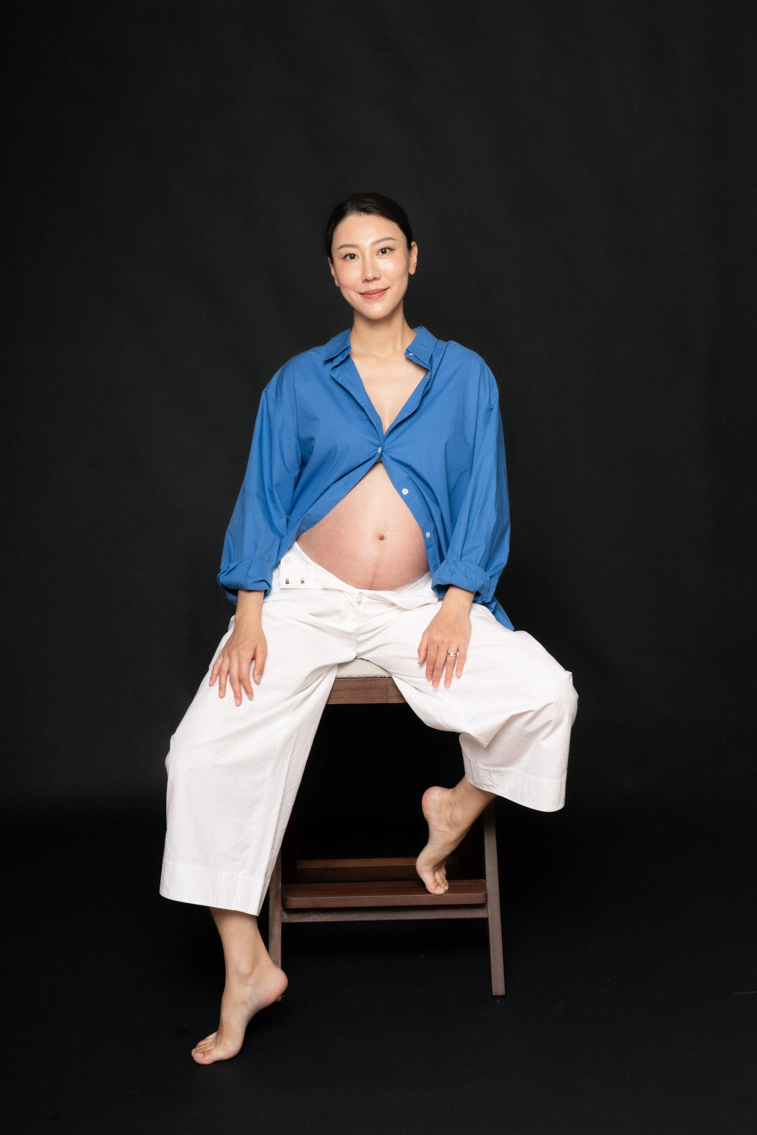 Cloris sitting on a high chair and showing off her baby bump in soft studio light