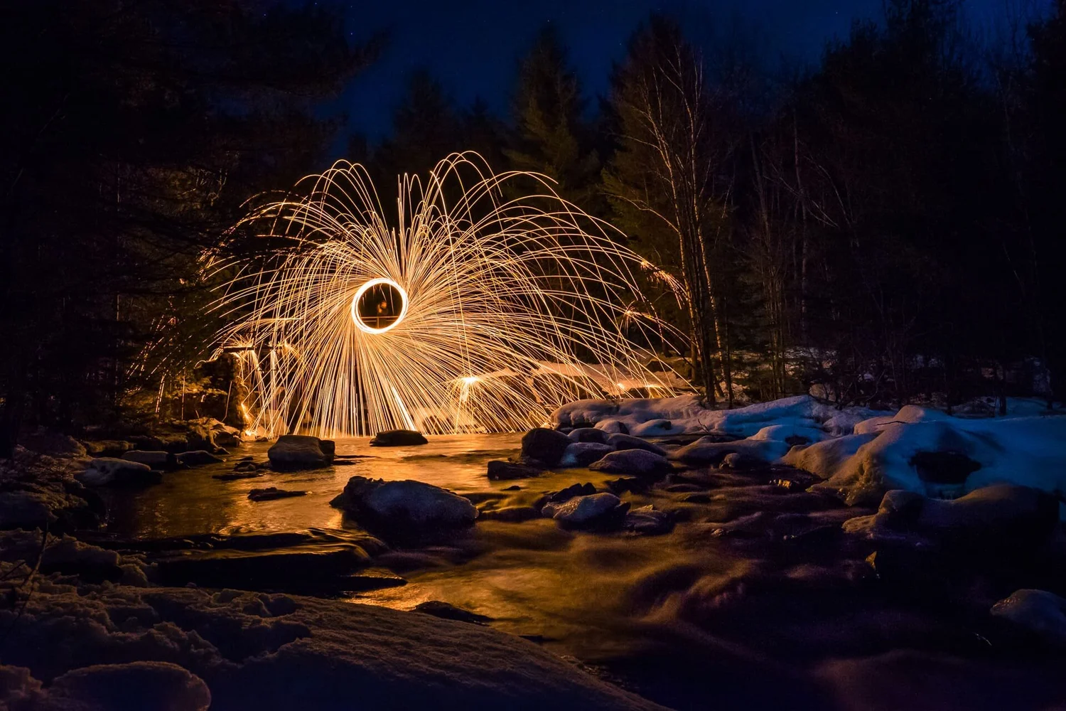 Steel wool spinning long exposure photography — sparks over a winter creek