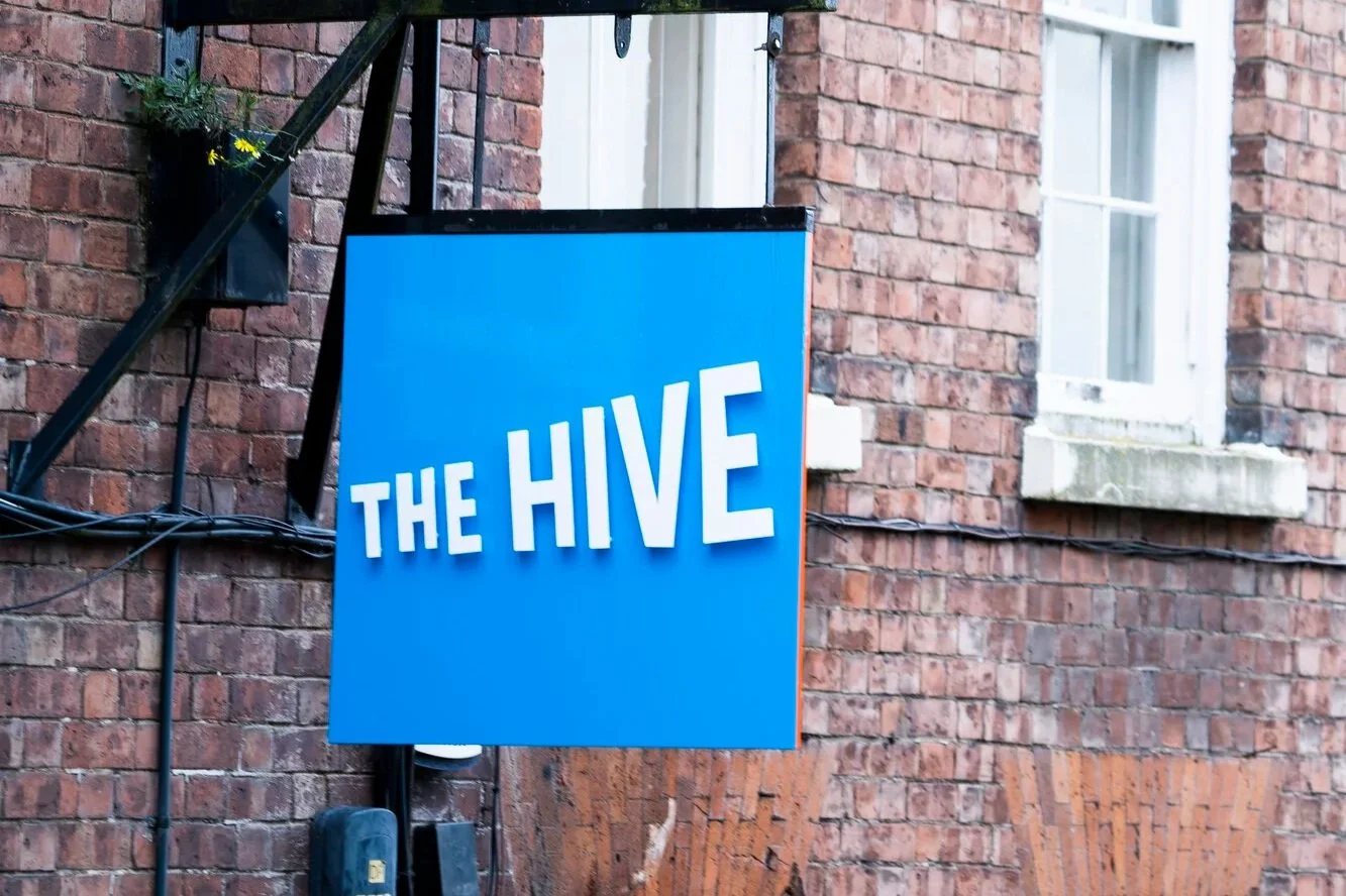 A closeup on The Hive's outdoor sign. The sign square, blue and The Hive is written across it in standout lettering.
