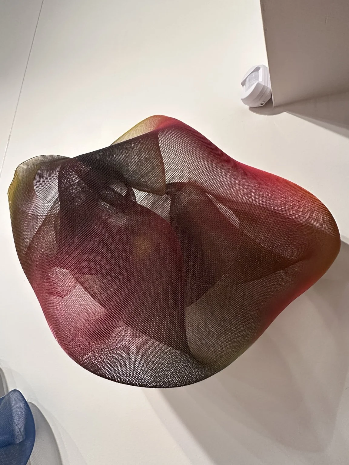 Burgundy translucent mesh wall sculpture creating folded volume and shadow.
