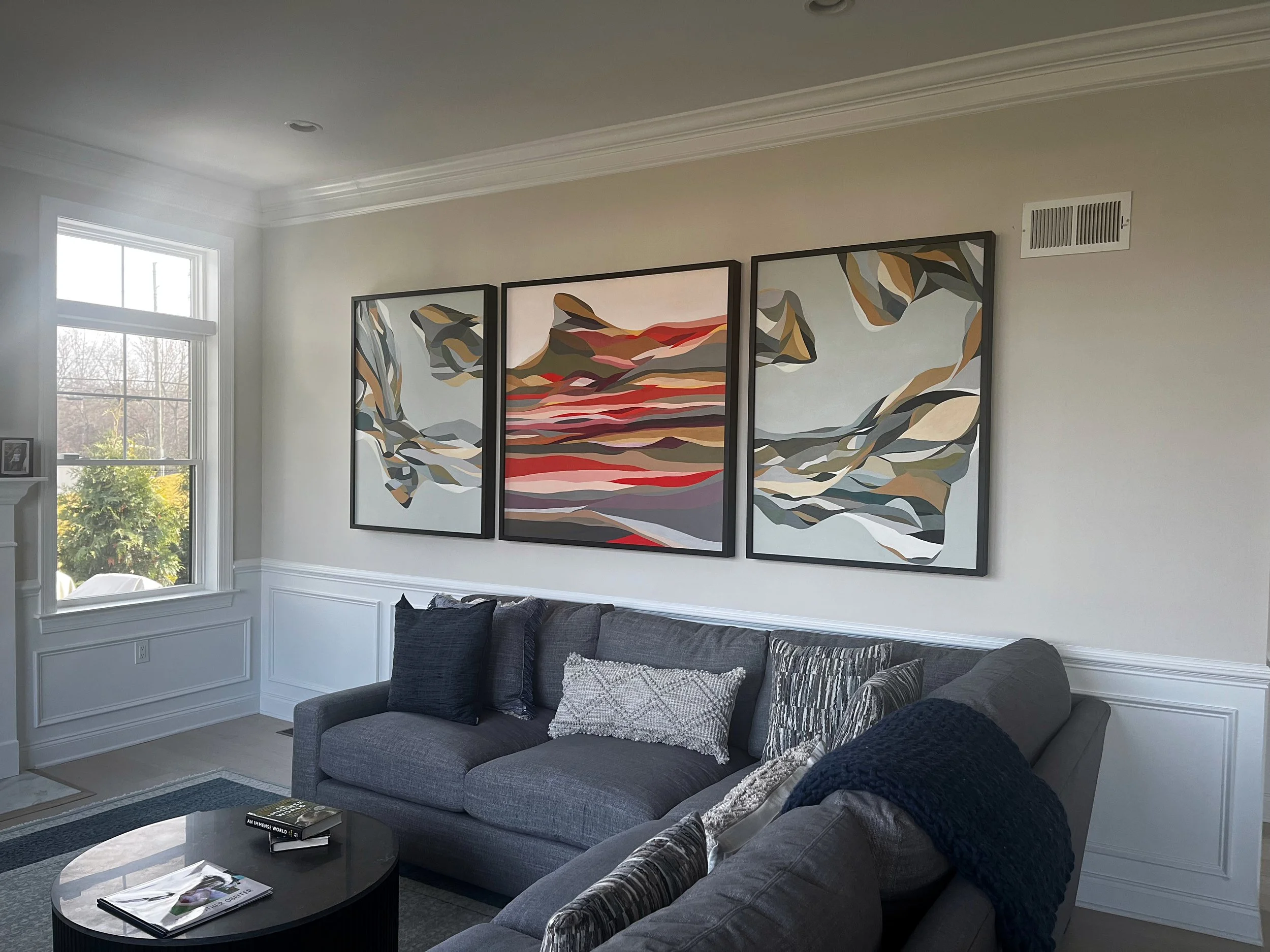 Modern living room featuring a large abstract triptych artwork above a gray sofa, demonstrating how statement wall art anchors contemporary interior design.