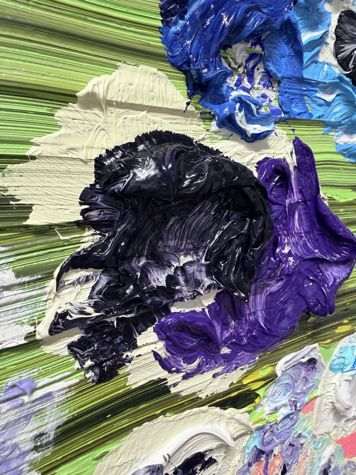 Close-up of thick impasto paint in black, purple, blue and cream over a green painted surface.