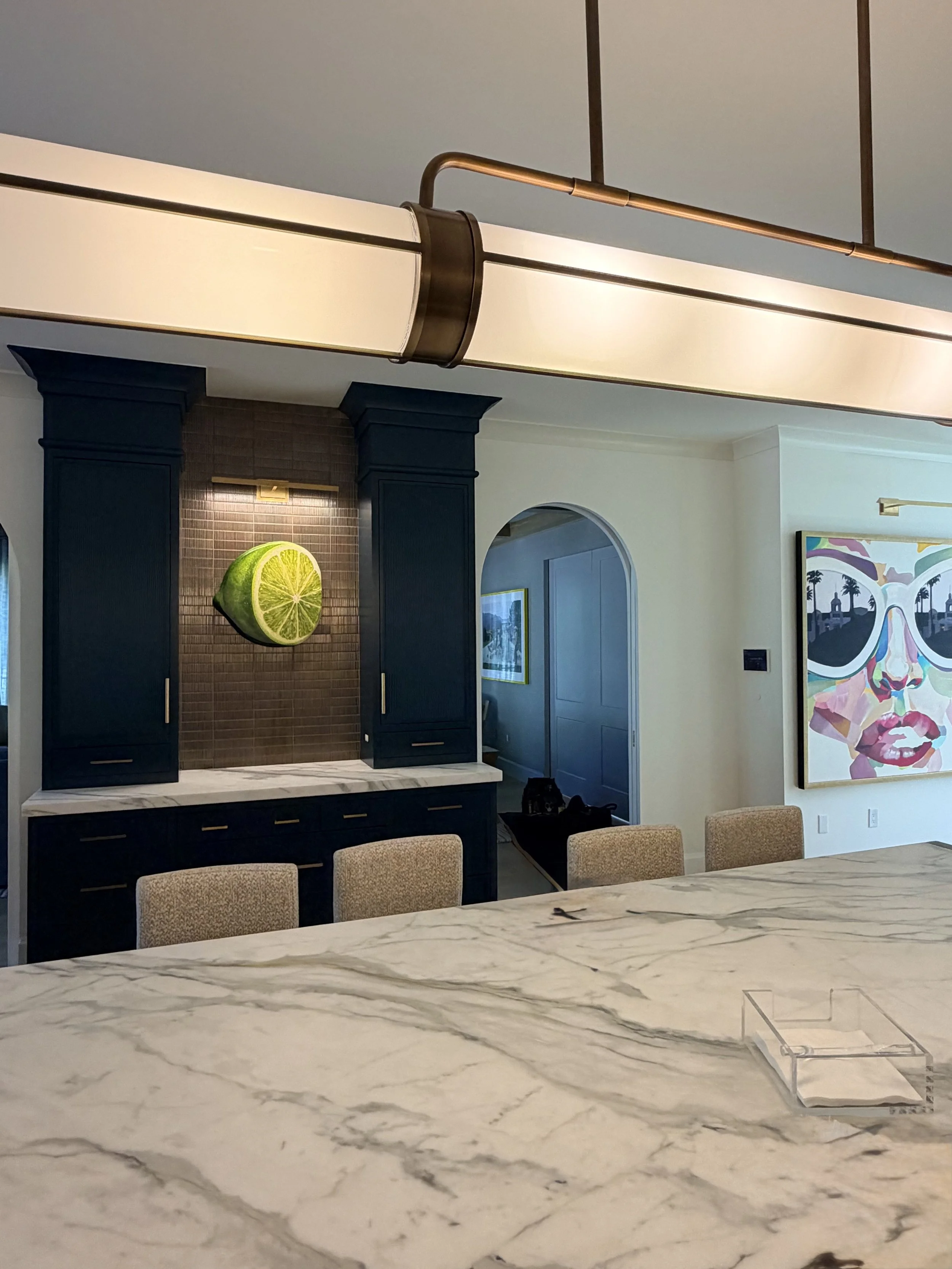 Contemporary lime artwork and a colorful portrait displayed in a kitchen with dark cabinets and a marble island.