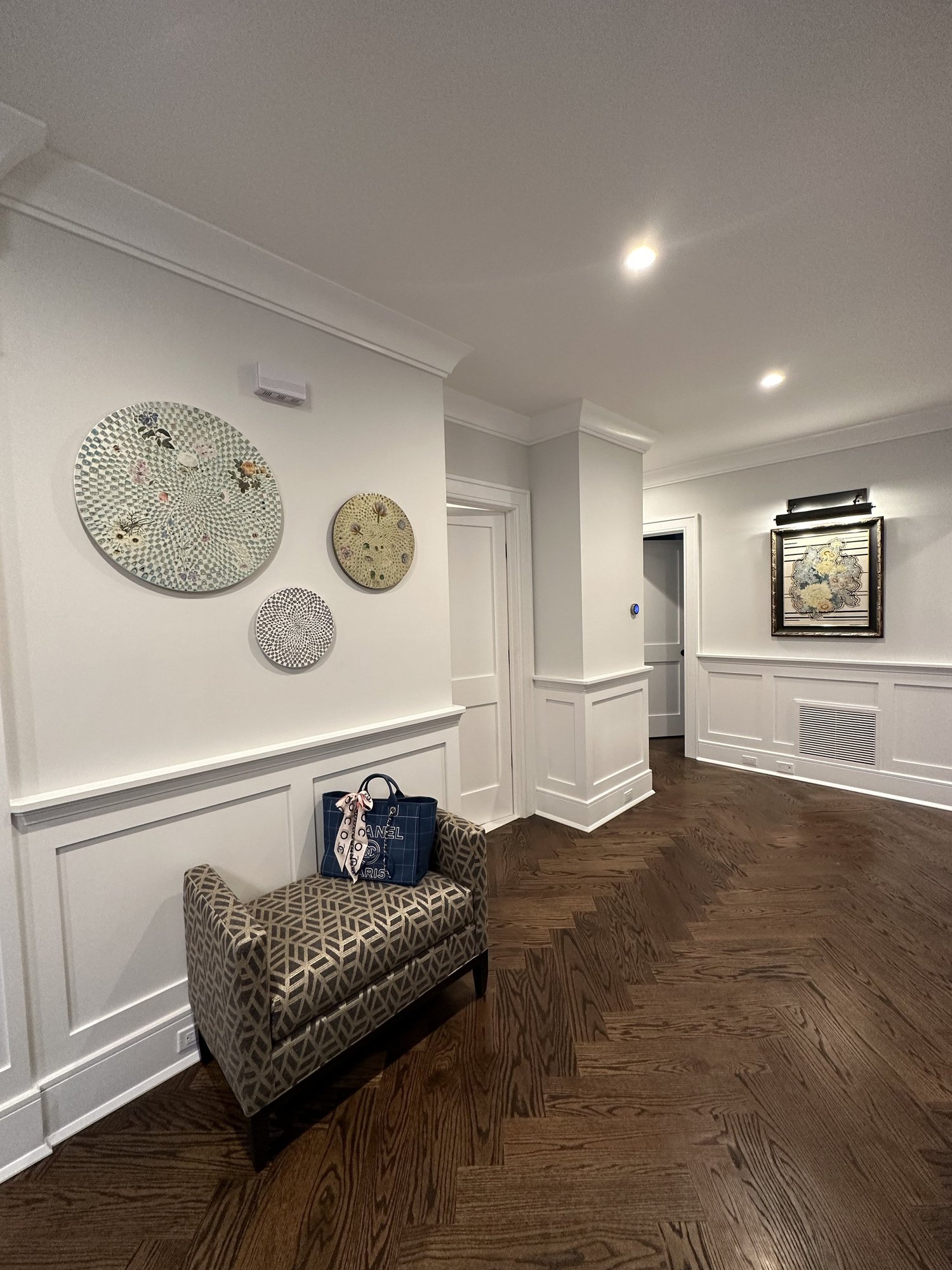 Three circular artworks by Jean Rim shown from an angle on a residential entryway wall above a patterned bench.