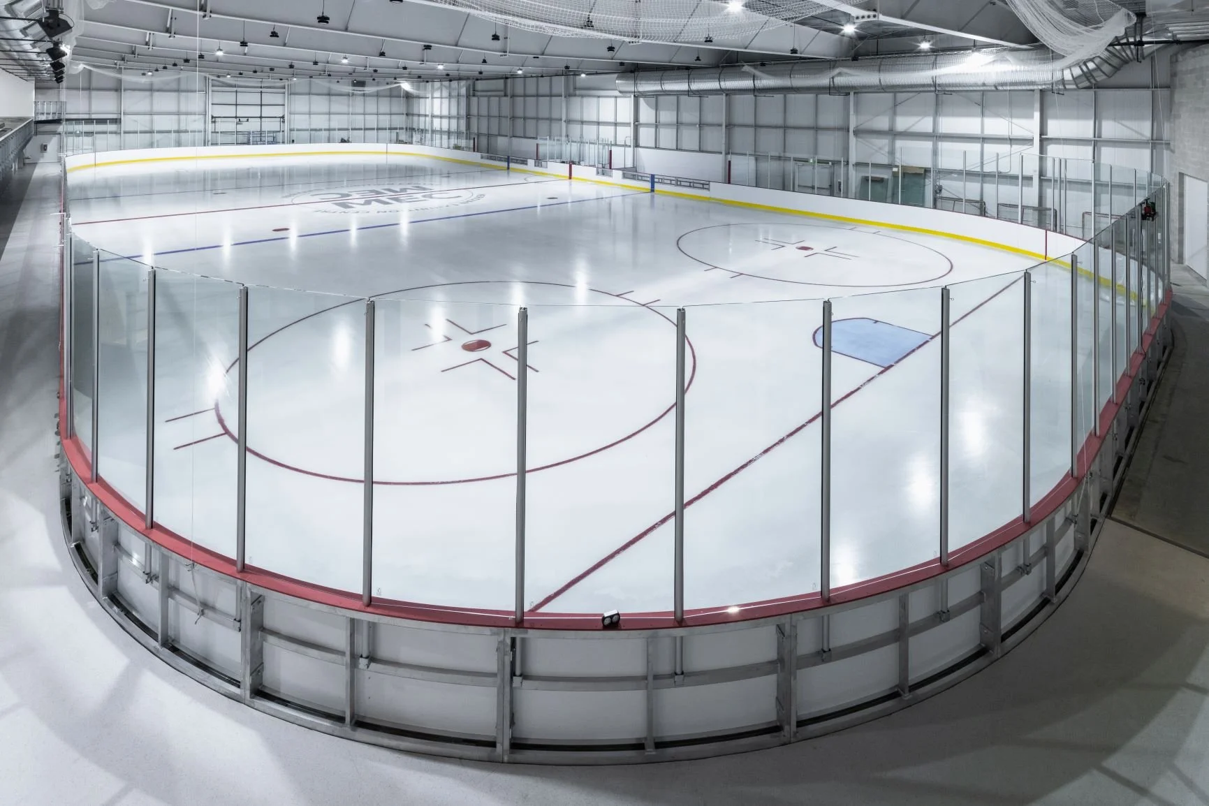 Empty indoor ice hockey rink with protective glass barriers and bright overhead lighting.