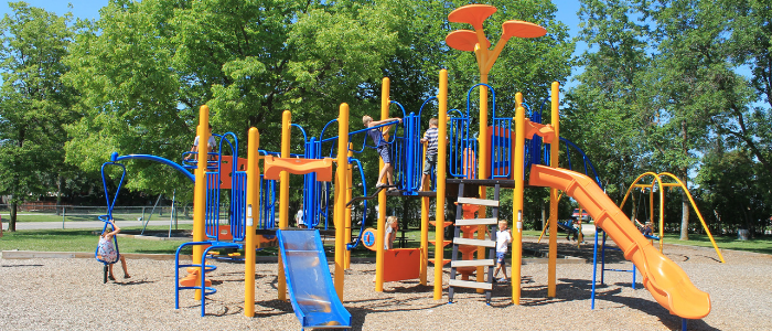 Children playing on a colorful playground with slides, climbing structures, and swings in a park.