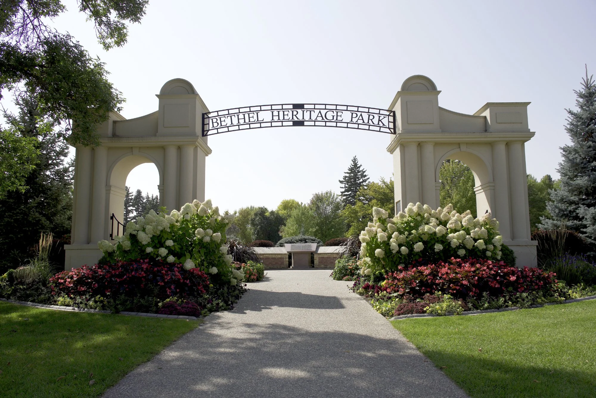 Entrance archway with a sign that reads 'Bethel Heritage Park' surrounded by lush greenery and colorful flowers.