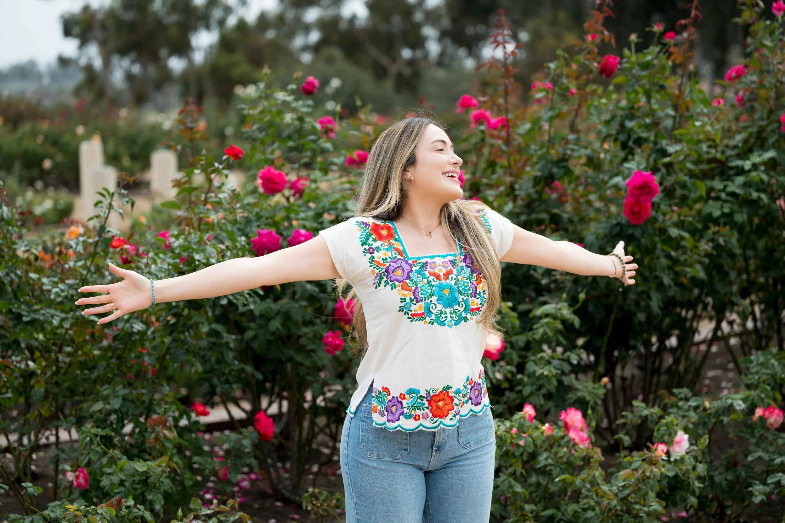 Woman smiling with open arms in Balboa Park's rose garden, captured during a photoshoot in San Diego