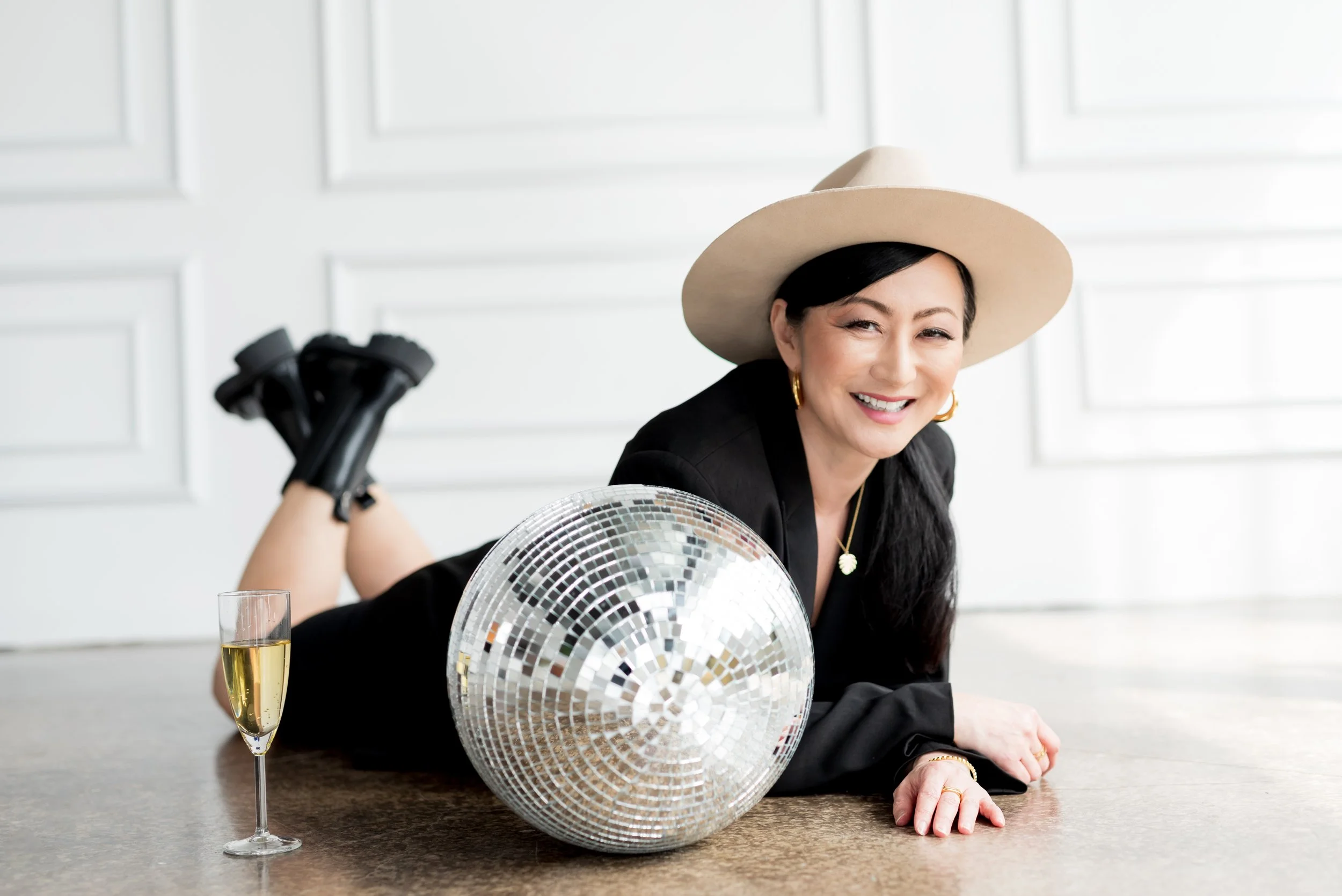 Professional woman celebrating with champagne next to a disco ball during a San Diego studio photoshoot