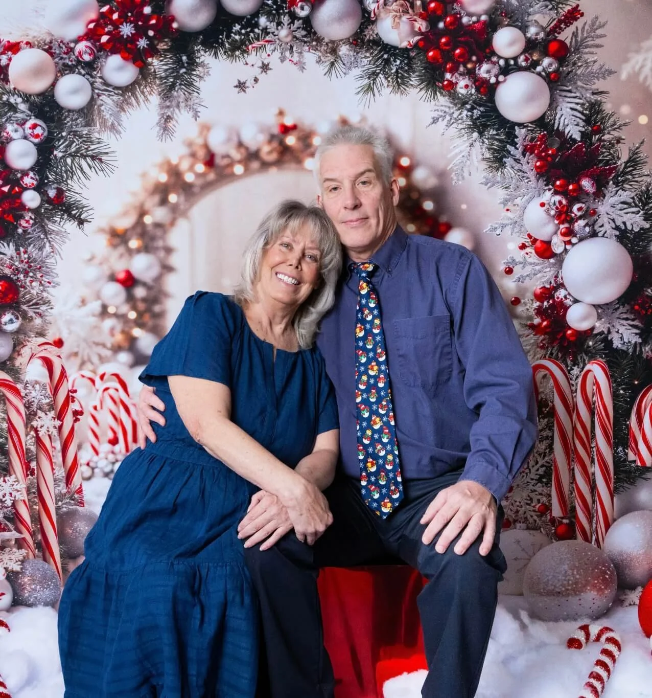 Randy and Kim seated together in front of red and white Christmas decorations.
