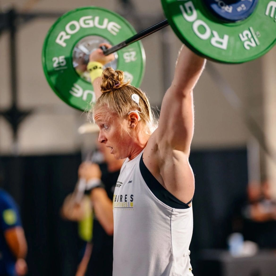 Woman lifting a barbell with green weights during a workout in a gym.