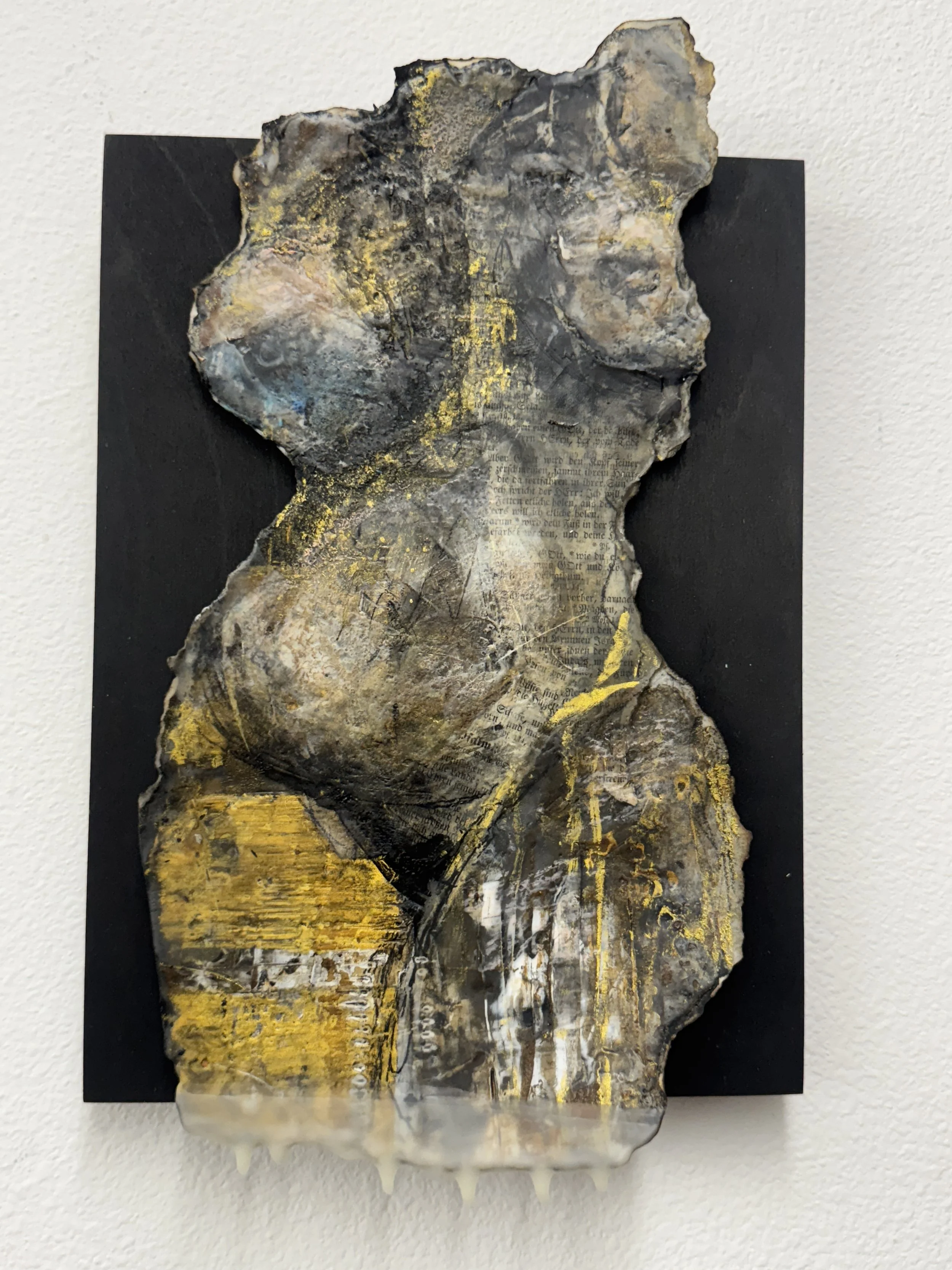 Mixed media artwork featuring a layered, textured abstract female torso with hints of text, paint, and gold accents on black background.