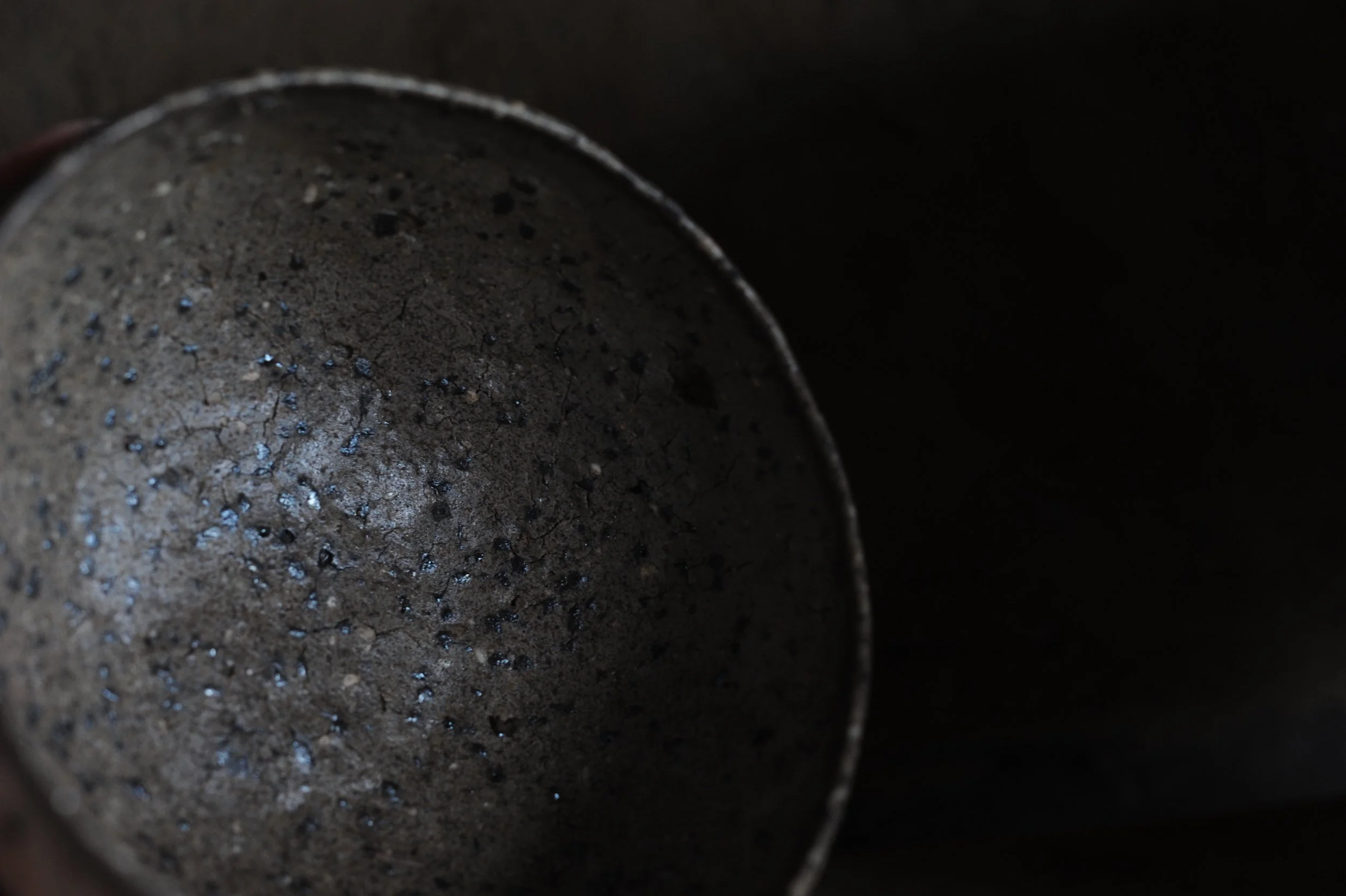 A close-up view of a metallic object with a rough, textured surface and black spots, possibly the inside of a container or pipe, against a dark background.
