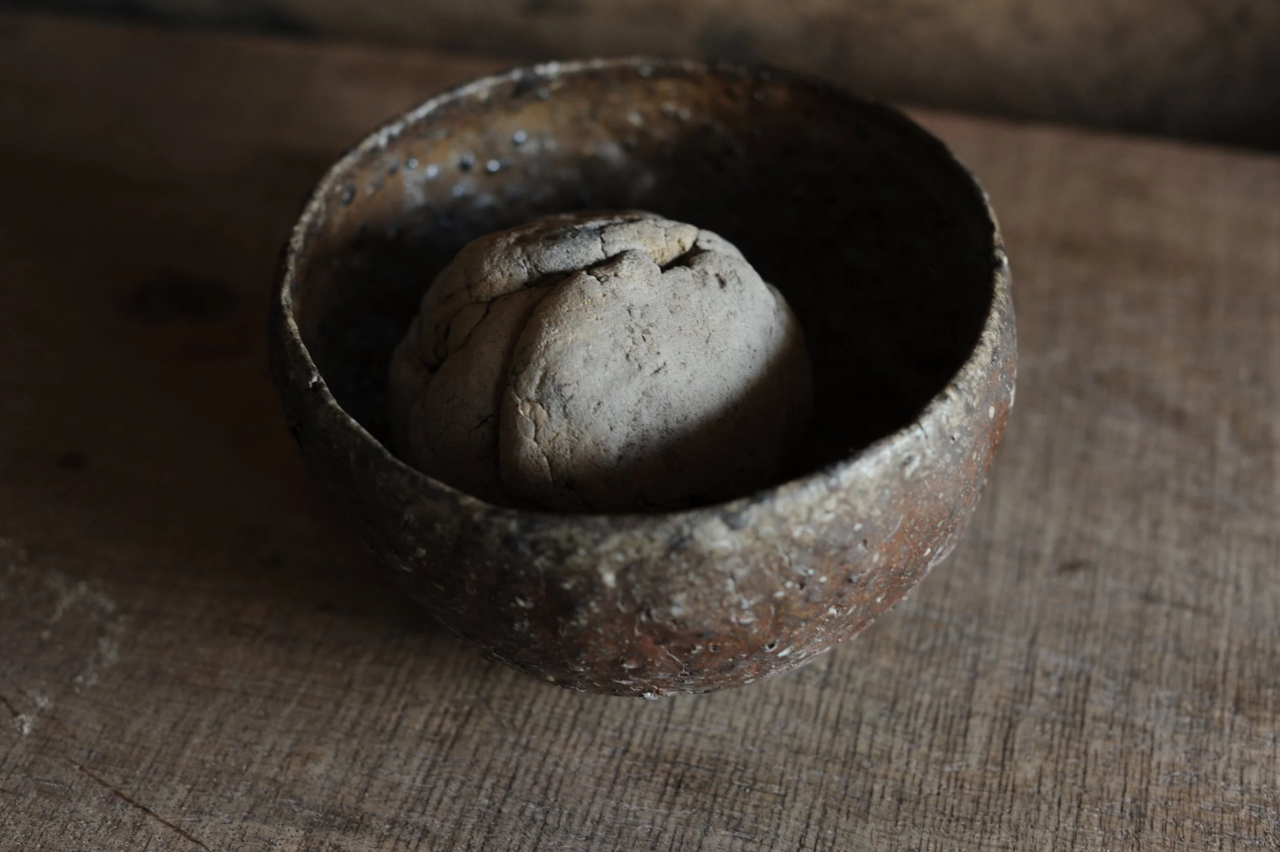 A rough, cracked stone placed inside a small, weathered ceramic bowl on a wooden surface.