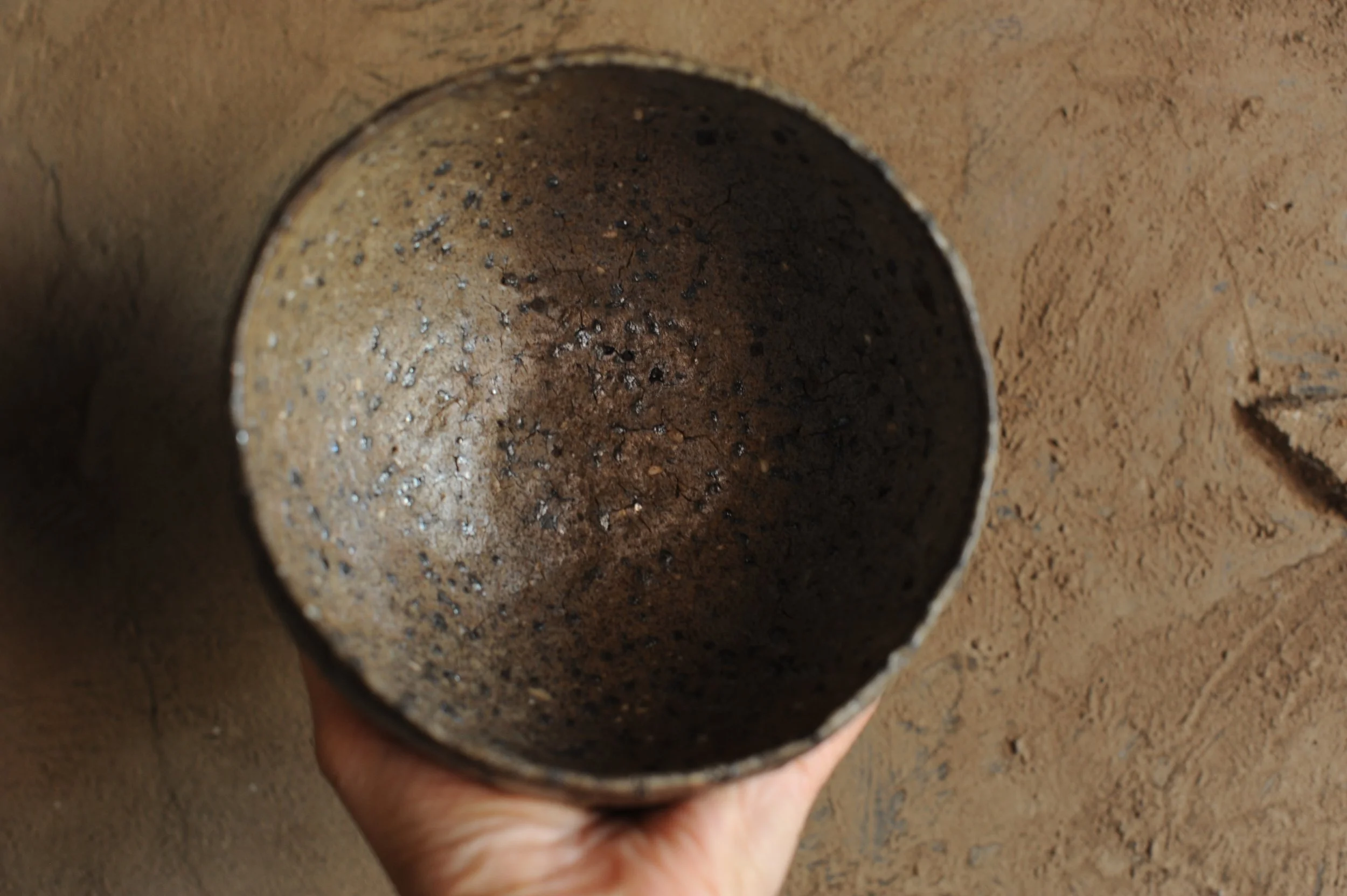 Close-up of a dusty, blackened metal pipe or cylinder with a rough, textured surface, held by a person's hand against a brown, sandy background.