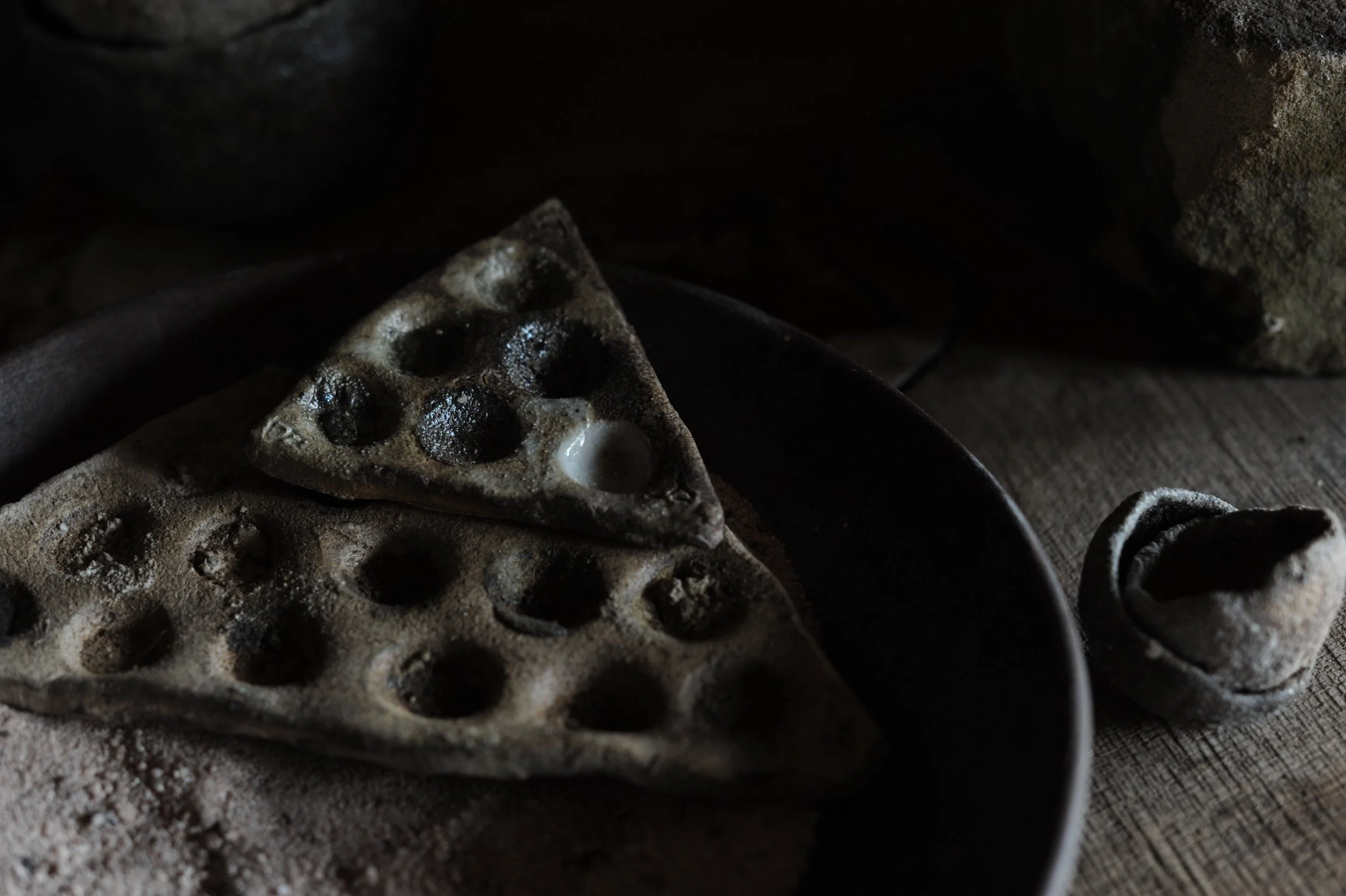 Two pieces of used, dusty waffle iron with a piece of waffle inside, on a dark plate, on a wooden surface with a rolled-up cloth nearby.