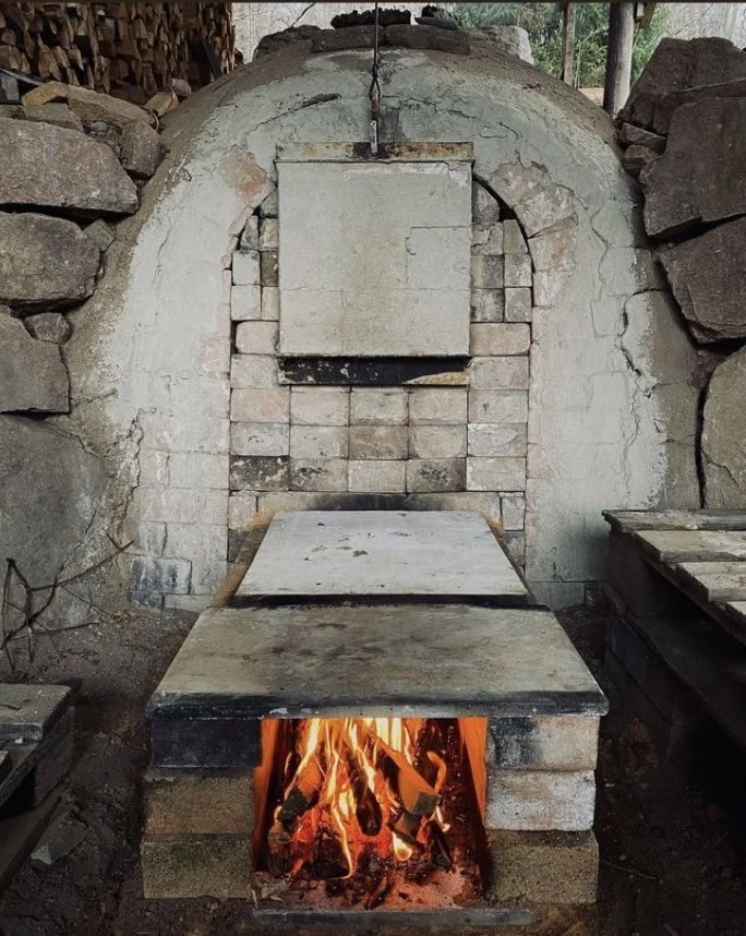An outdoor brick oven with a wood fire burning in the front, surrounded by stacked stones and bricks.
