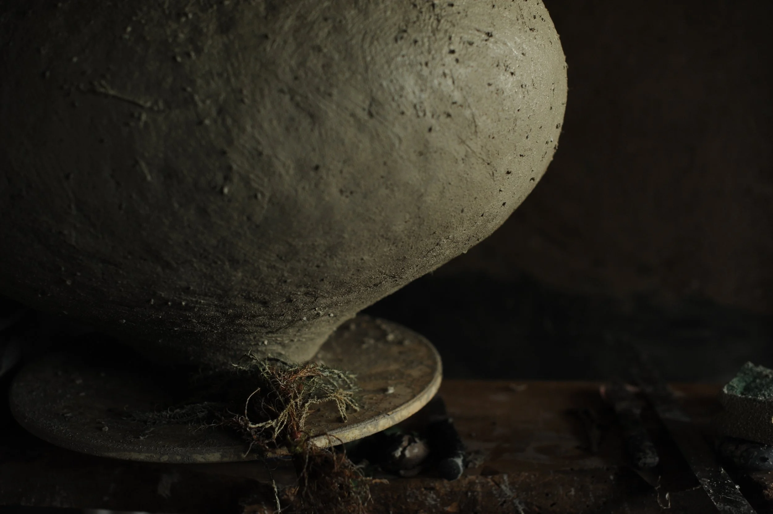 Close up of a dusty and dirty mortar and pestle on a wooden surface with some plant roots and debris nearby.
